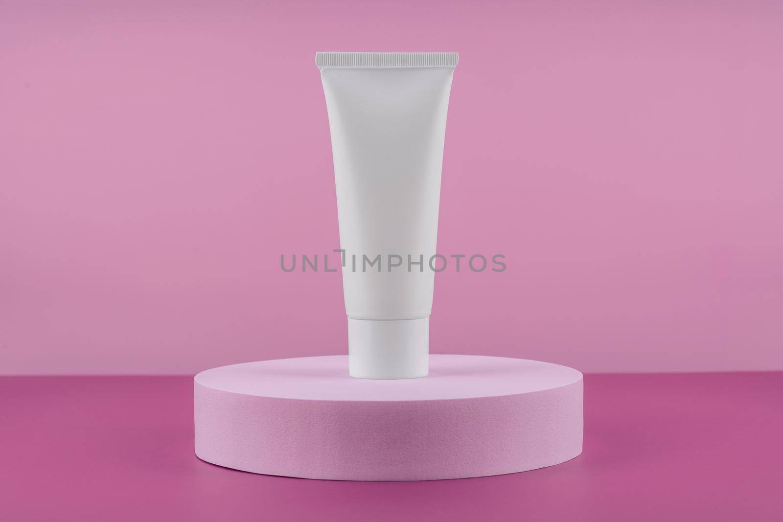 White tube of cosmetic product on podium pedestal on pink background. Cream bottle, lotion, mousse showcase for skincare routine. Beauty cleanser, shampoo stand. by photolime