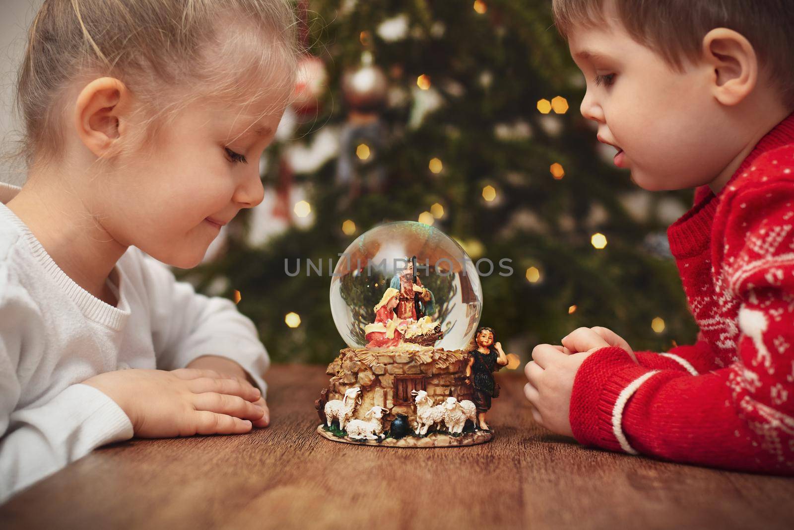 Children looking at a glass ball with a scene of the birth of Jesus Christ near christmas tree