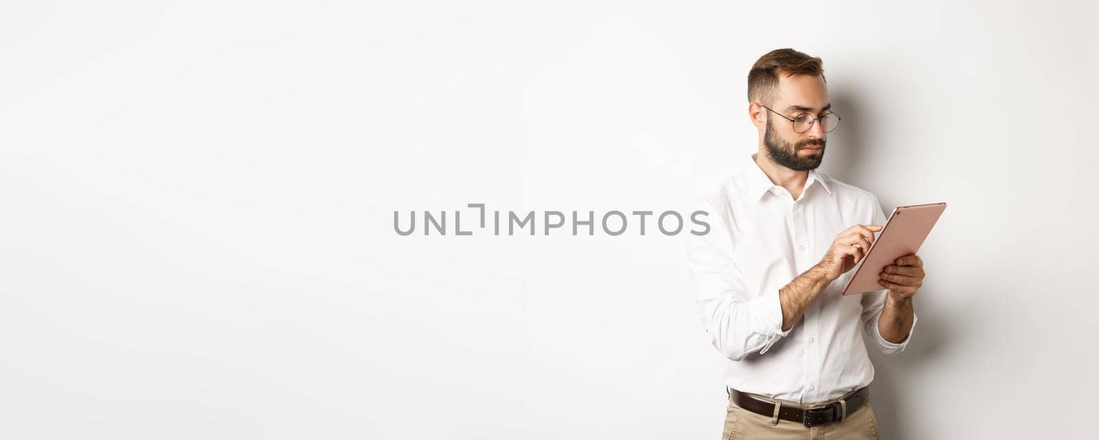 Businessman working on digital tablet, looking busy, standing over white background.