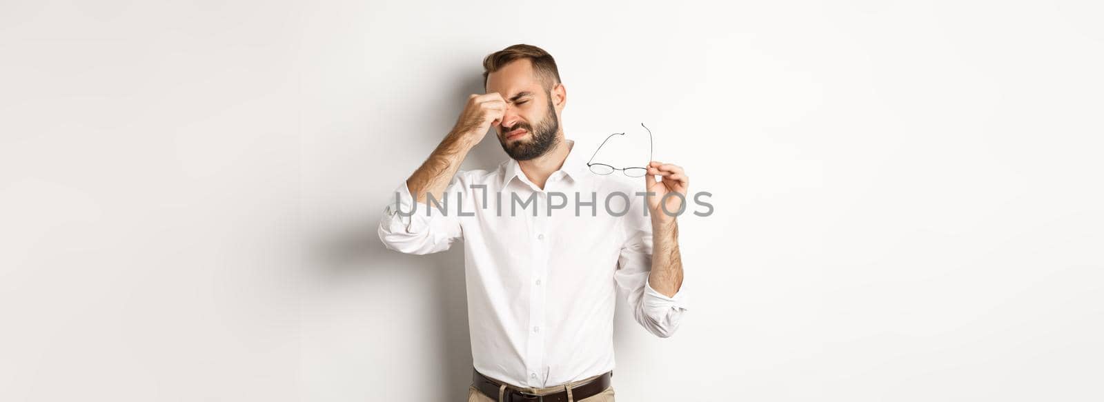 Tired businessman take-off glasses and rubbing eyes, standing exhausted against white background by Benzoix