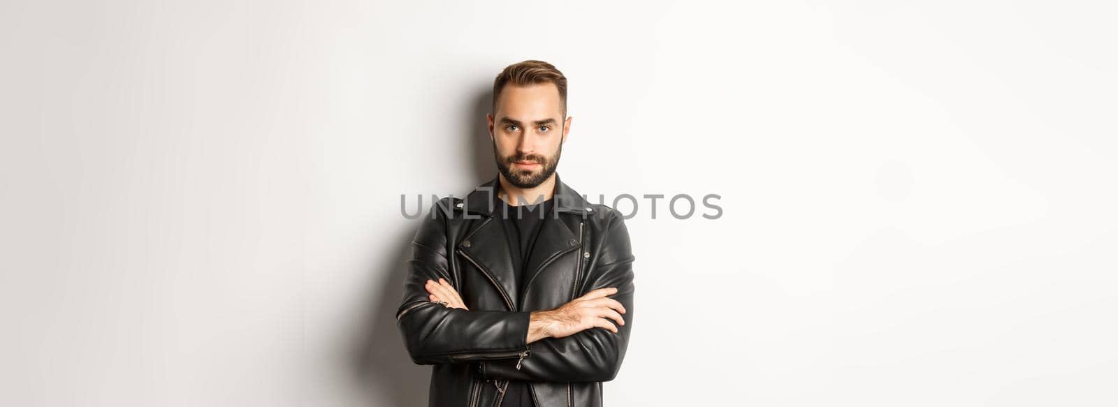 Handsome man wearing leather jacket, looking confident at camera, standing over white background.