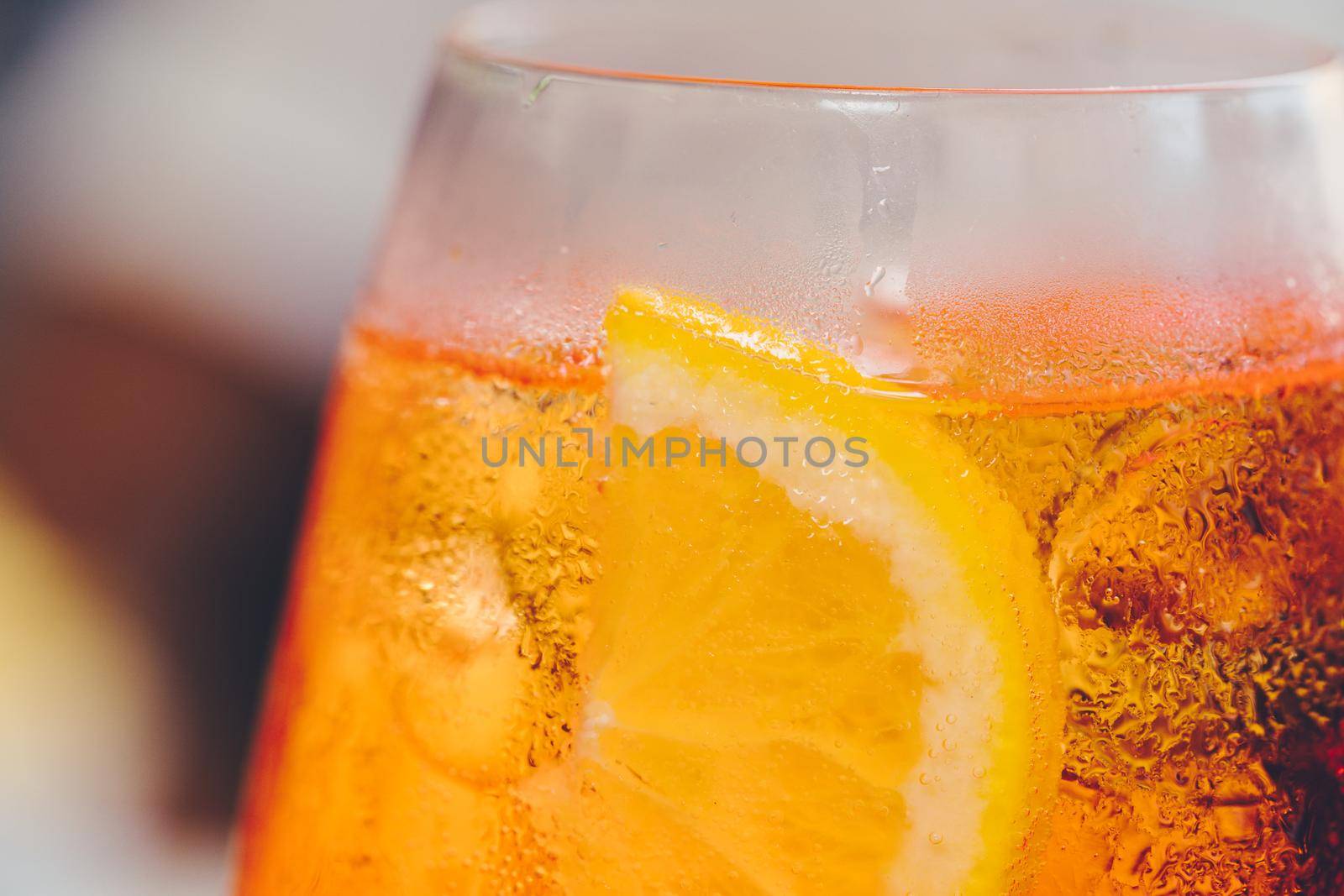 Glass of ice cold Aperol spritz cocktail served in a wine glass, decorated with slices of orange. Aperitif in street caffe in Italy. Macro by photolime