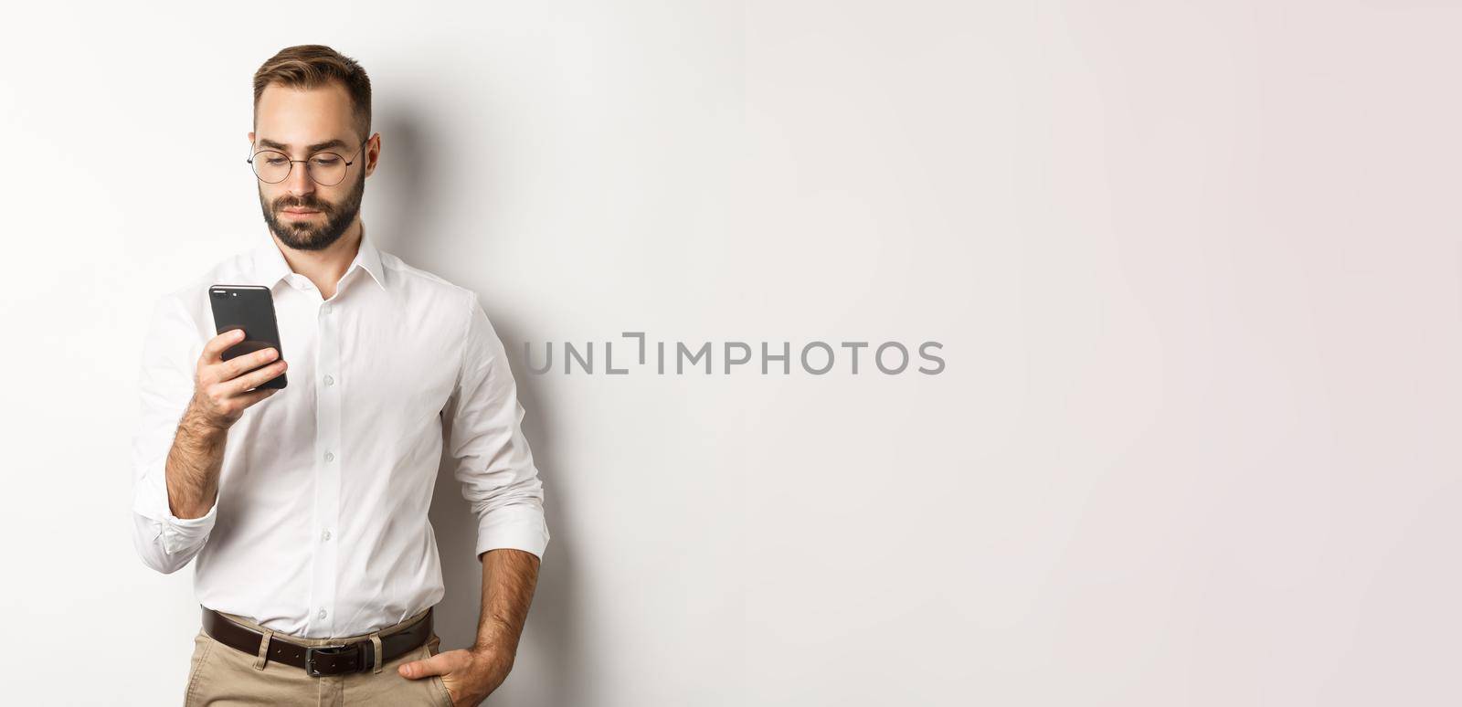 Businessman reading message on phone, standing over white background.