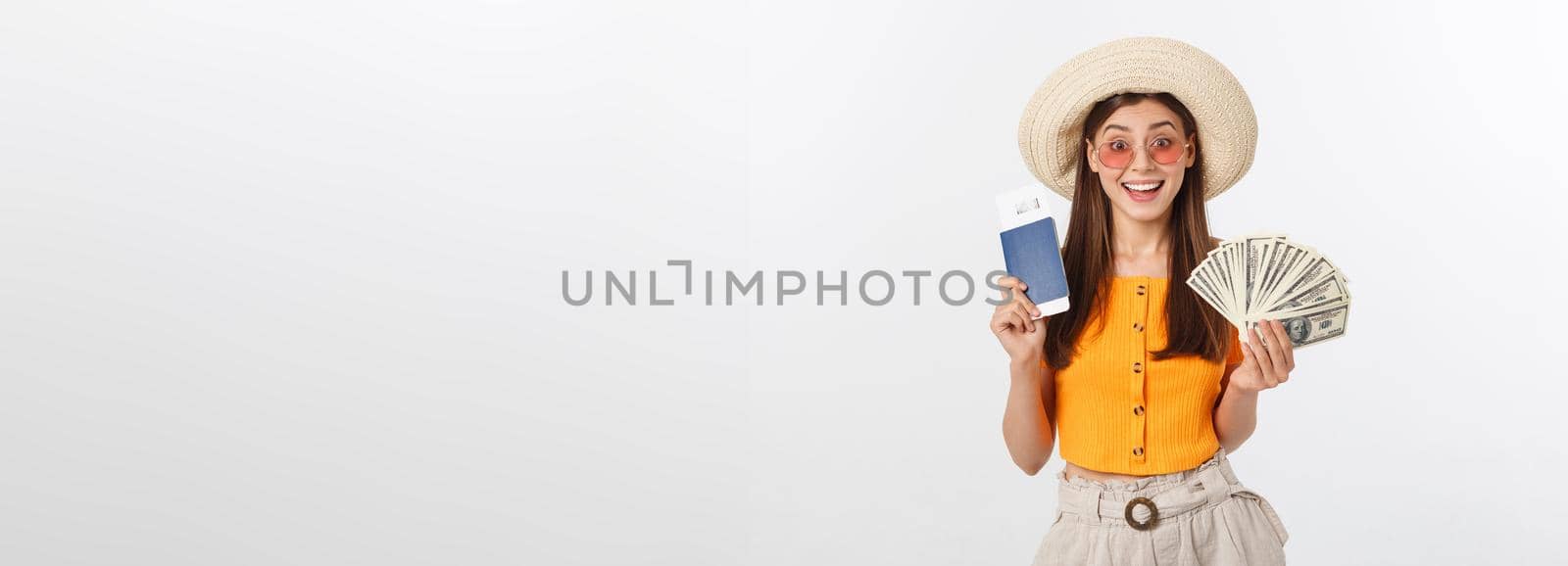 Portrait of cheerful, happy, laughing girl with hat on head, having money fan and passport with tickets in hands, isolated on white background.