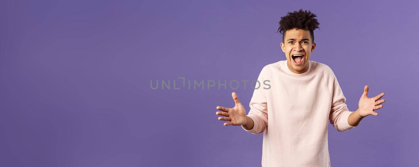 Portrait of concerned, upset and frustrated young man cant believe he lost, asking why, spread hands sideways in dismay, complaining shouting angry and uneasy, standing purple background.