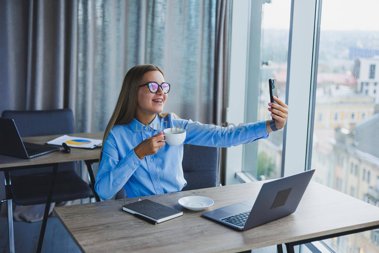 Smart female employee with netbook looking at camera during mobile call, successful freelancer in jacket talking on phone via app