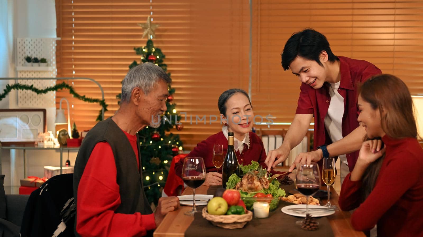 Young coupler celebrating Christmas or New Year with grandparents at cozy home. Holidays and celebration concept.