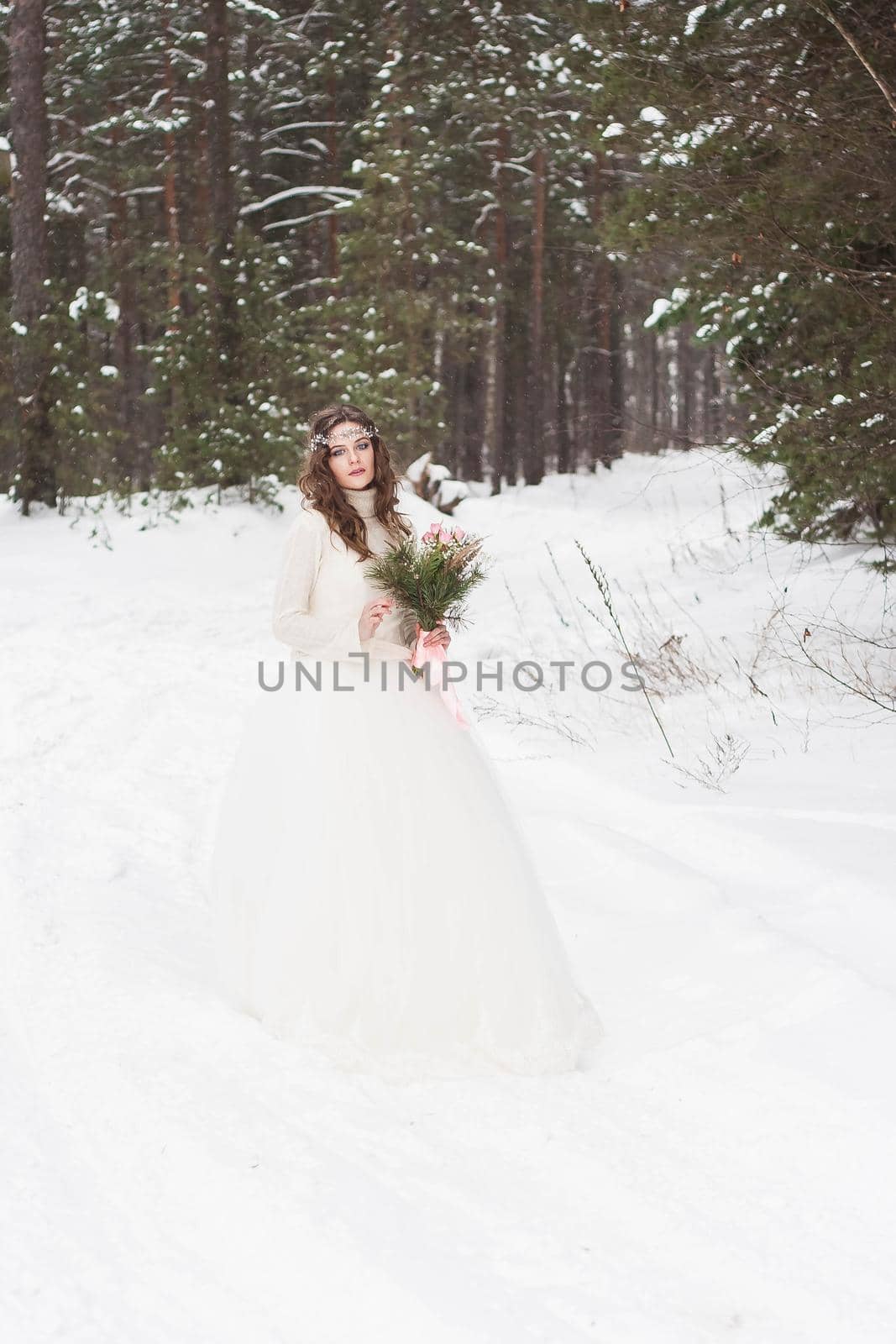 Beautiful bride in a white dress with a bouquet in a snow-covered winter forest. Portrait of the bride in nature.