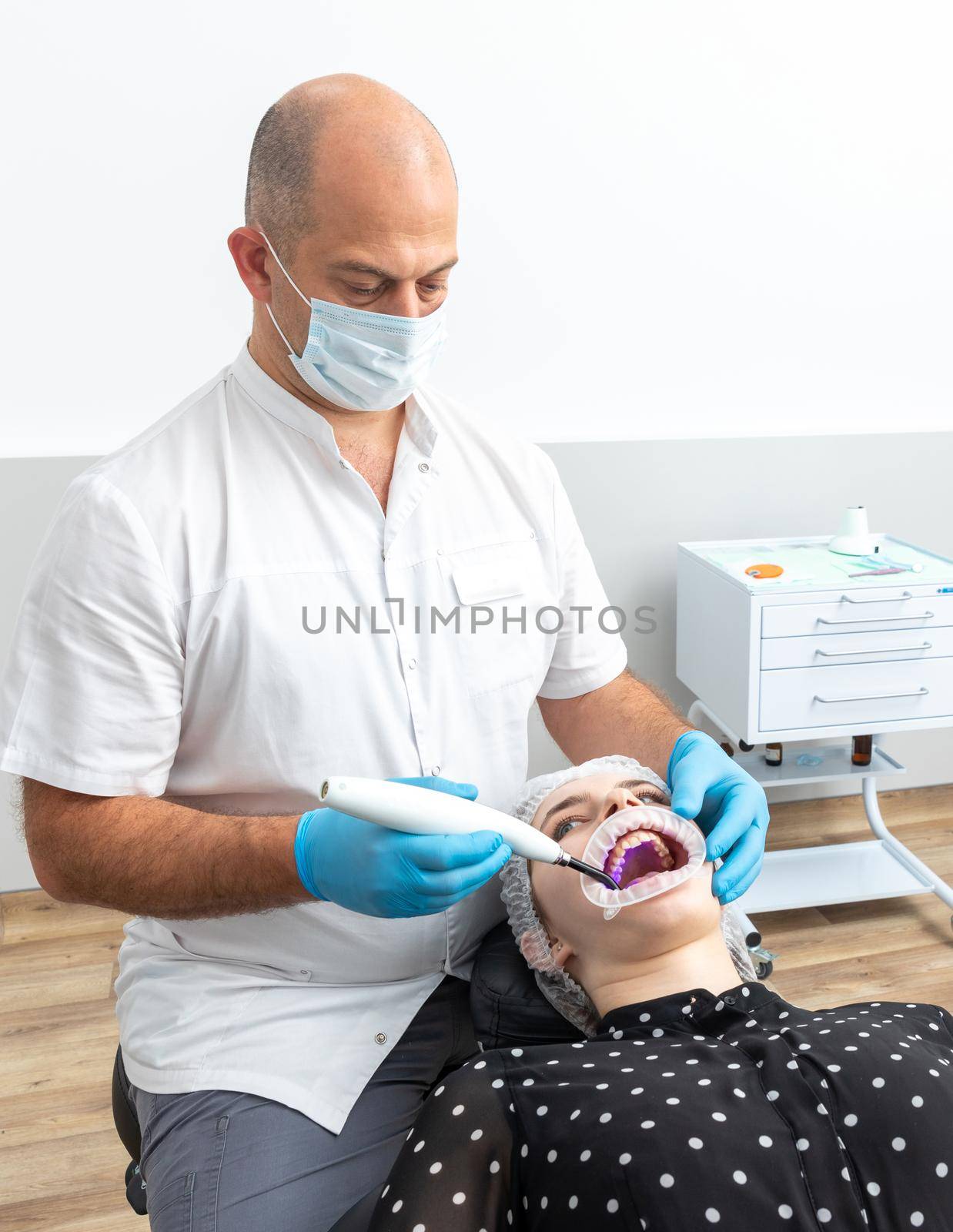 Dentist using dental curing UV lamp on teeth of patient by Mariakray