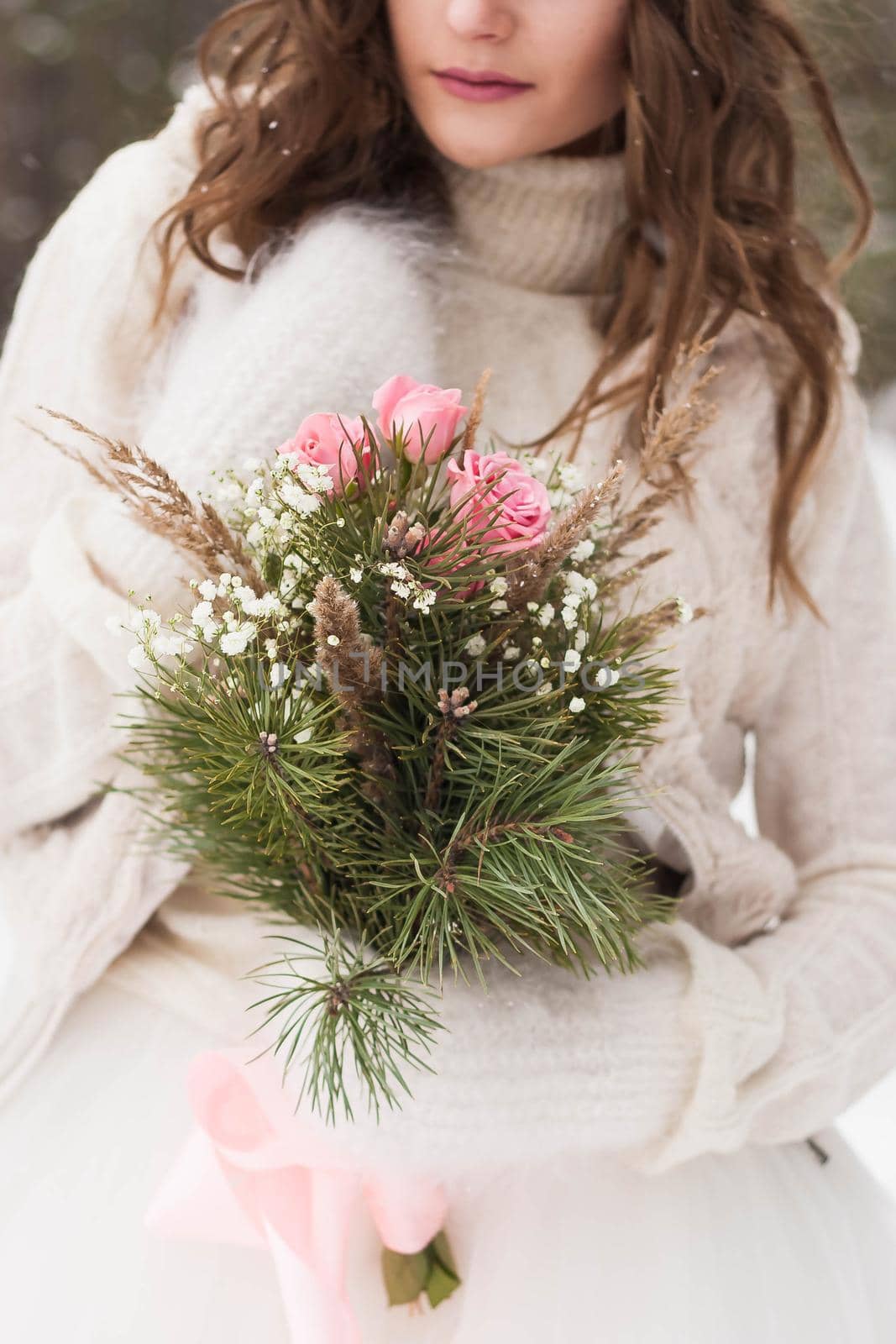 Beautiful bride in a white dress with a bouquet in a snow-covered winter forest. Portrait of the bride in nature.