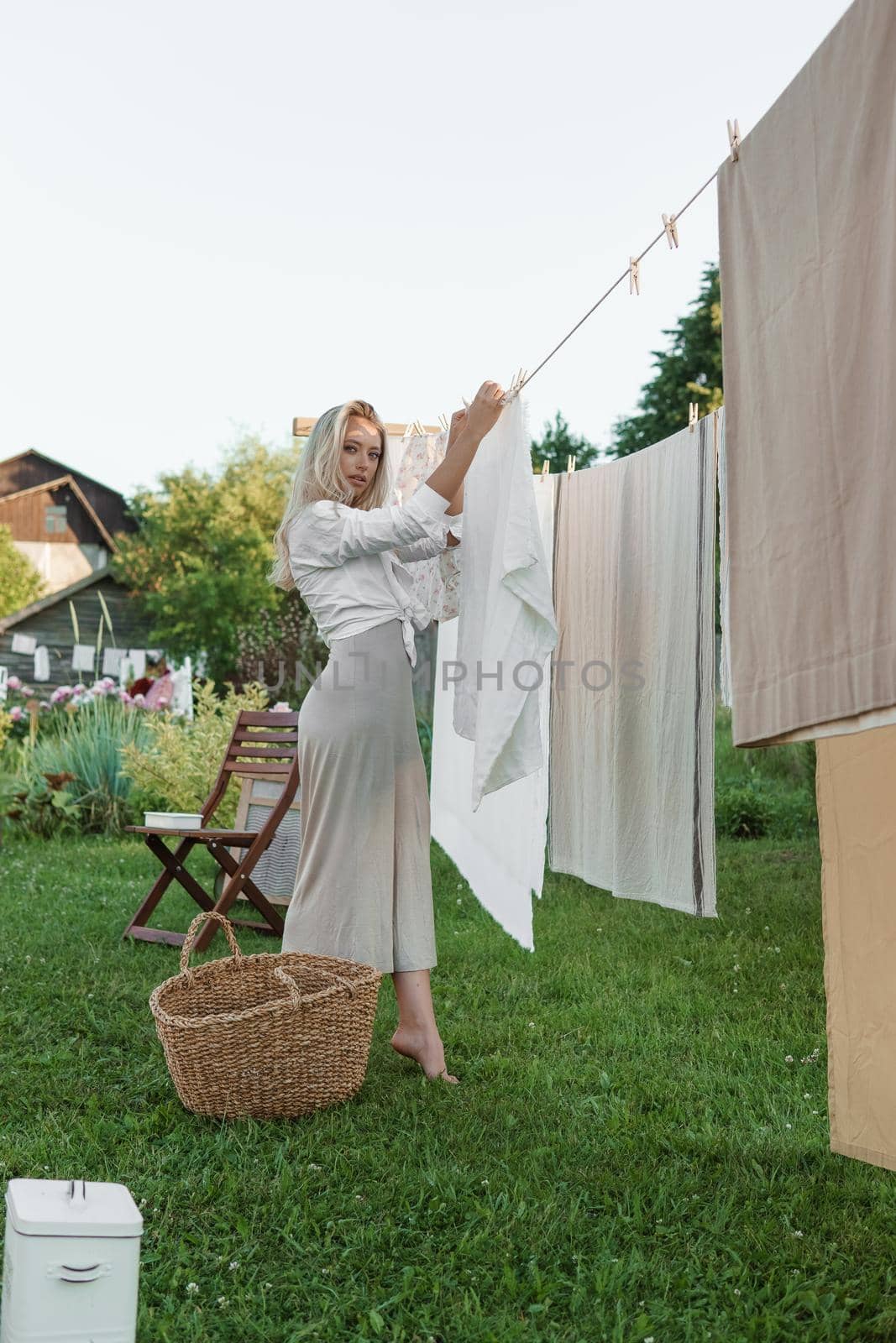 Laundry day. A woman hangs linen and towels on a tree in the courtyard of a village house. Summer cottage concept.