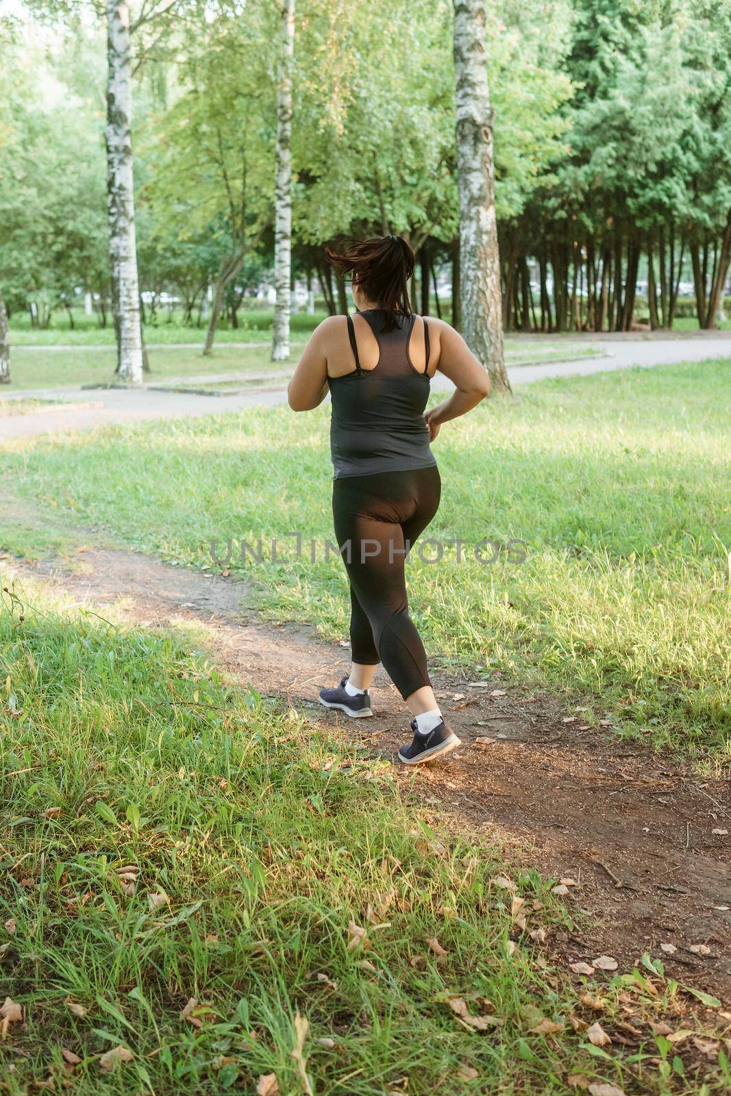 A charming brunette woman plus-size body positive practices sports in nature.