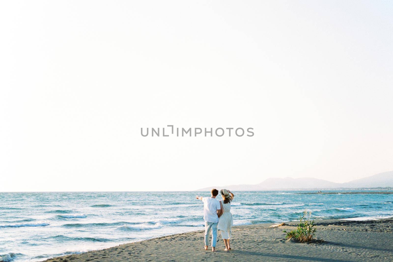 Man shows the sea with his finger to the woman, standing on the beach. Back view. High quality photo