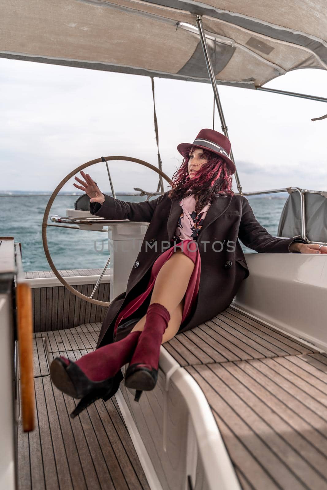 Attractive middle-aged woman at the helm of a yacht on a summer day. Luxury summer adventure, outdoor activities. by Matiunina
