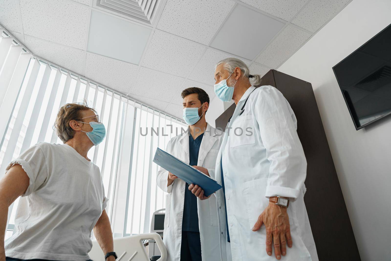 Doctors in masks explain to a sick patient in a wheelchair her diagnosis and treatment by Yaroslav_astakhov