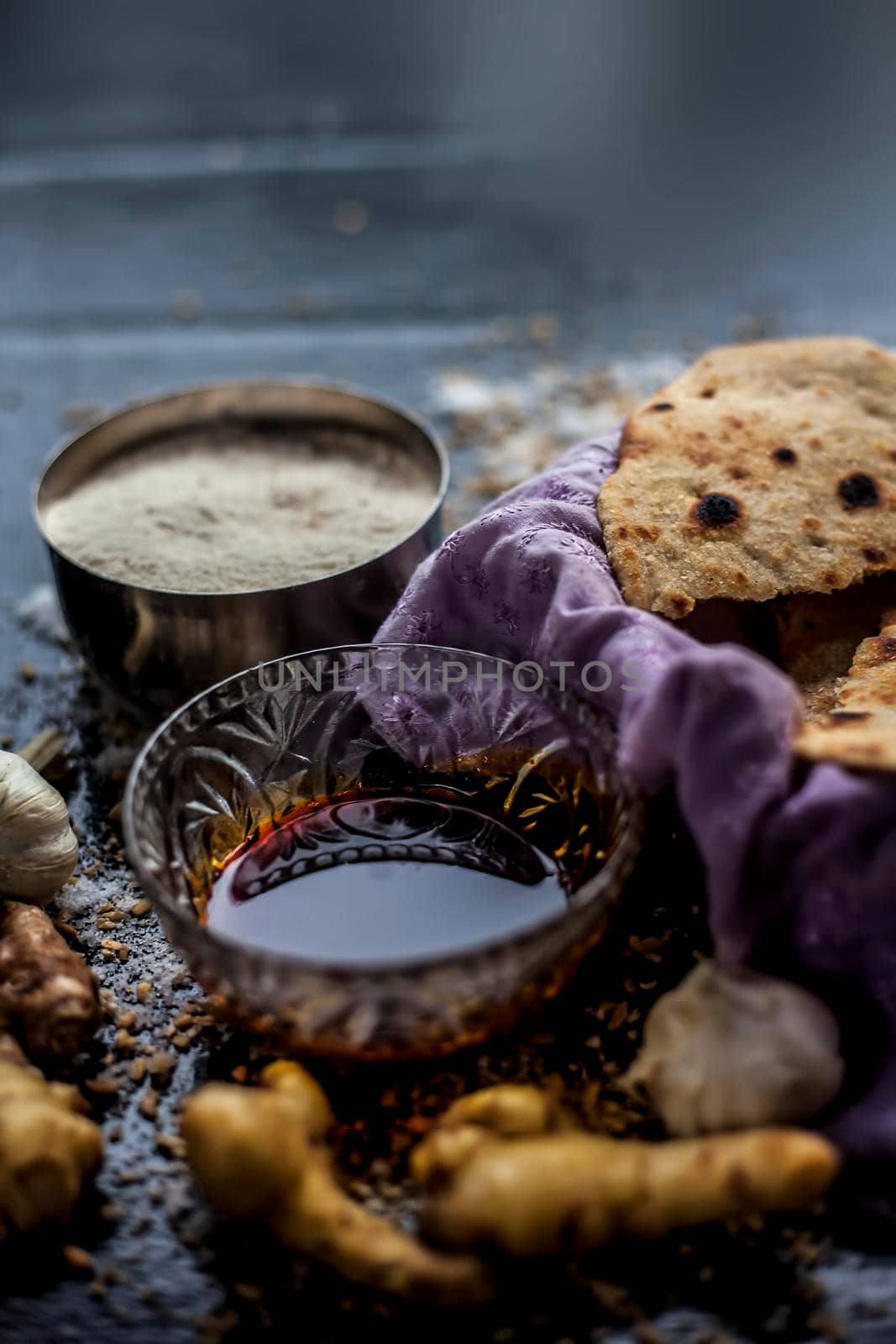 Shot of Gujarati breakfast consisting of round bread bhakri and lasun chutney. Shot of bhakhri, with wheat flour, garlic chutney, salt, ginger, and some whole wheat grains on a black glossy surface. by mirzamlk