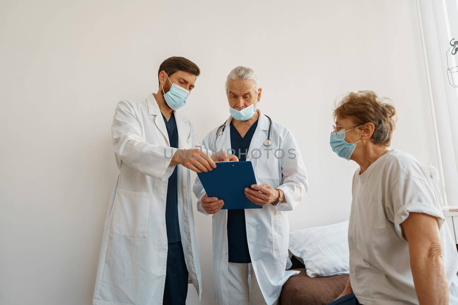 Doctors in masks explain to a sick patient in a wheelchair her diagnosis and treatment by Yaroslav_astakhov