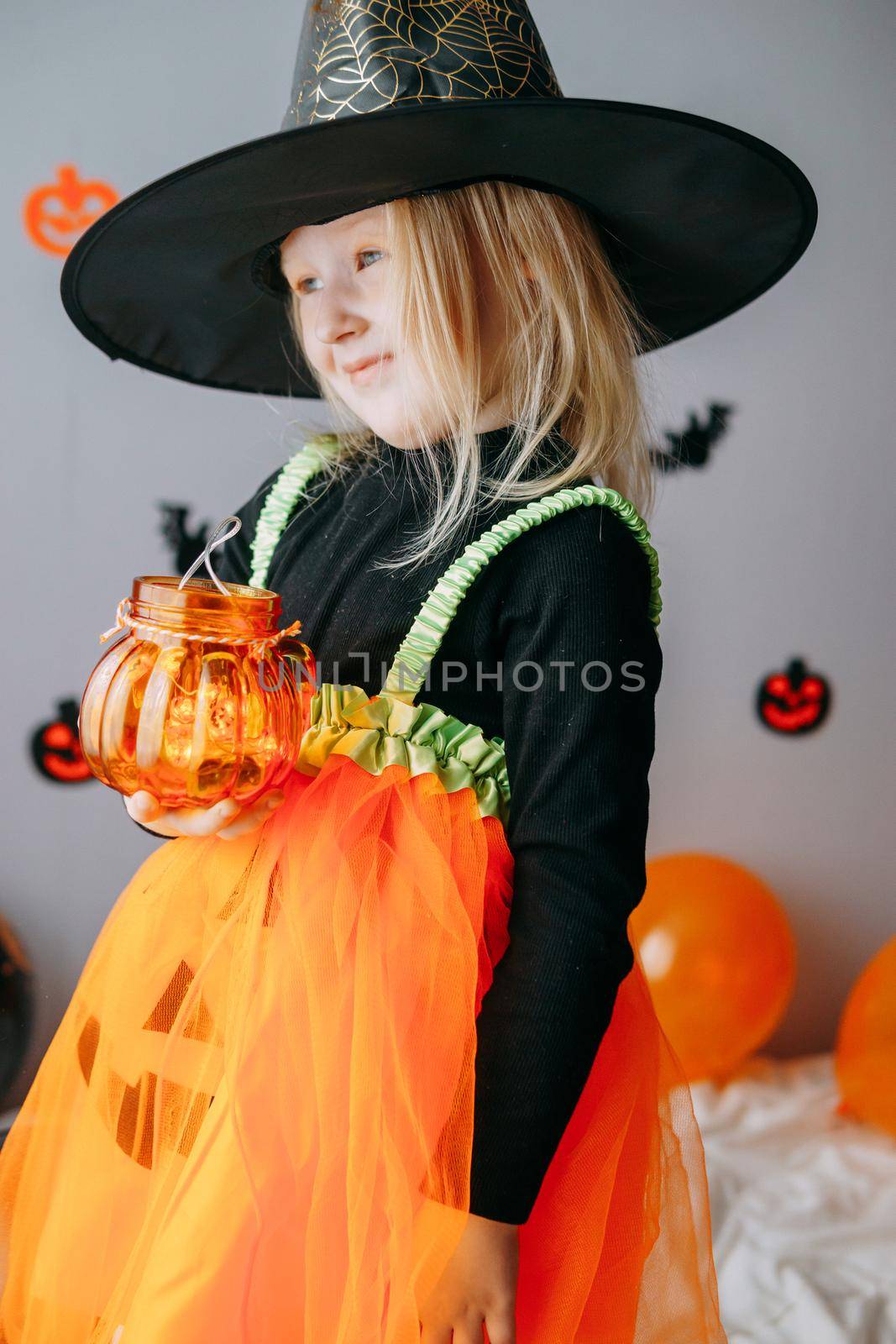 Children's Halloween - a girl in a witch hat and a carnival costume with airy orange and black balloons at home. Ready to celebrate Halloween.