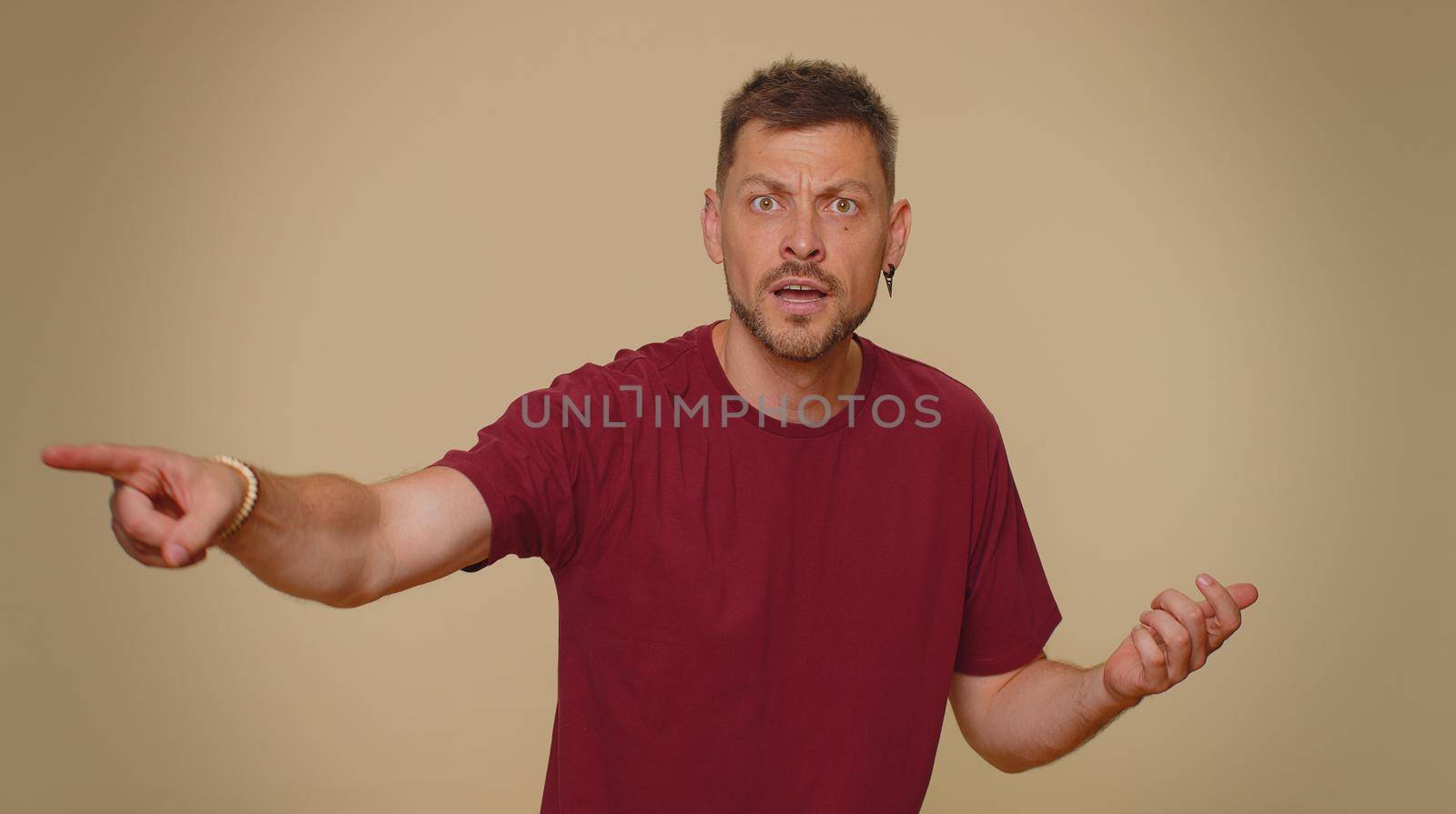 Get out of here. You are fired. Dissatisfied young man pointing finger away asking to leave his alone, strict boss firing, conflict, crisis, deadline. Adult stylish guy on beige studio wall background