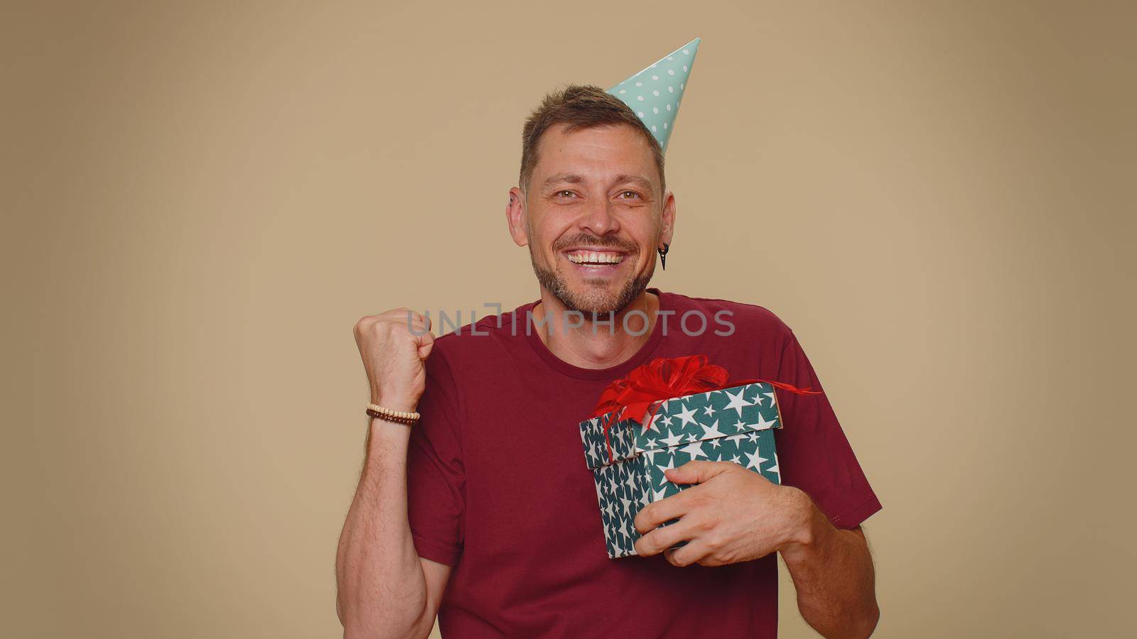 Cheerful bearded handsome young man receiving gift box and smiling joyfully, looking amazed satisfied with nice present, unexpected birthday surprise. Stylish male guy on beige studio background