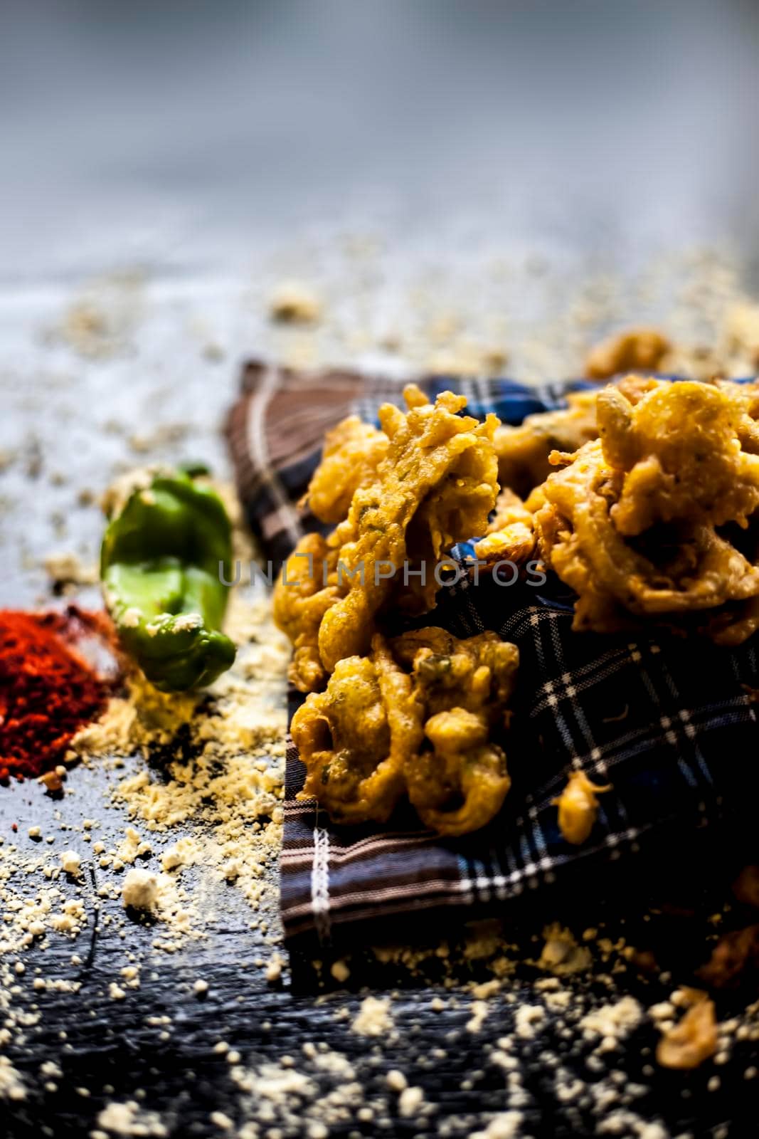 Famous kanda bhaji or kanda bhajiya or kanda pakora in a container on a black surface along with chickpea flour, spices, and all other ingredients for making it.