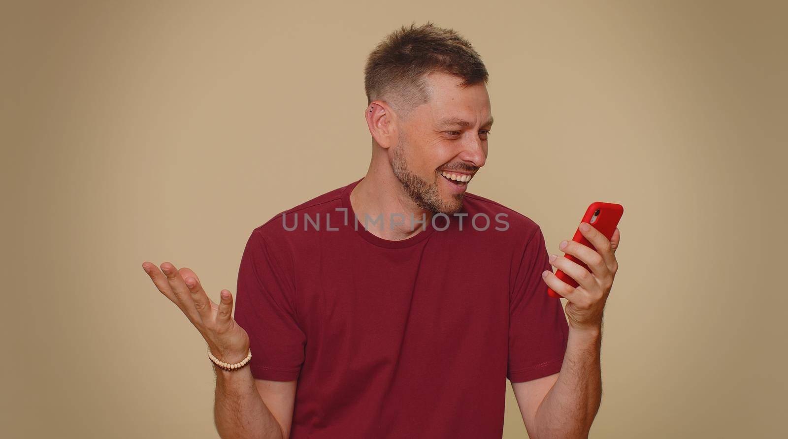Happy excited joyful young man use smartphone typing browsing say wow yes, found out great big win news doing winner gesture. Adult stylish male guy isolated on beige studio wall background indoors