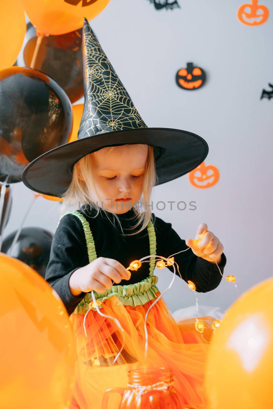 Children's Halloween - a girl in a witch hat and a carnival costume with airy orange and black balloons at home. Ready to celebrate Halloween by Annu1tochka