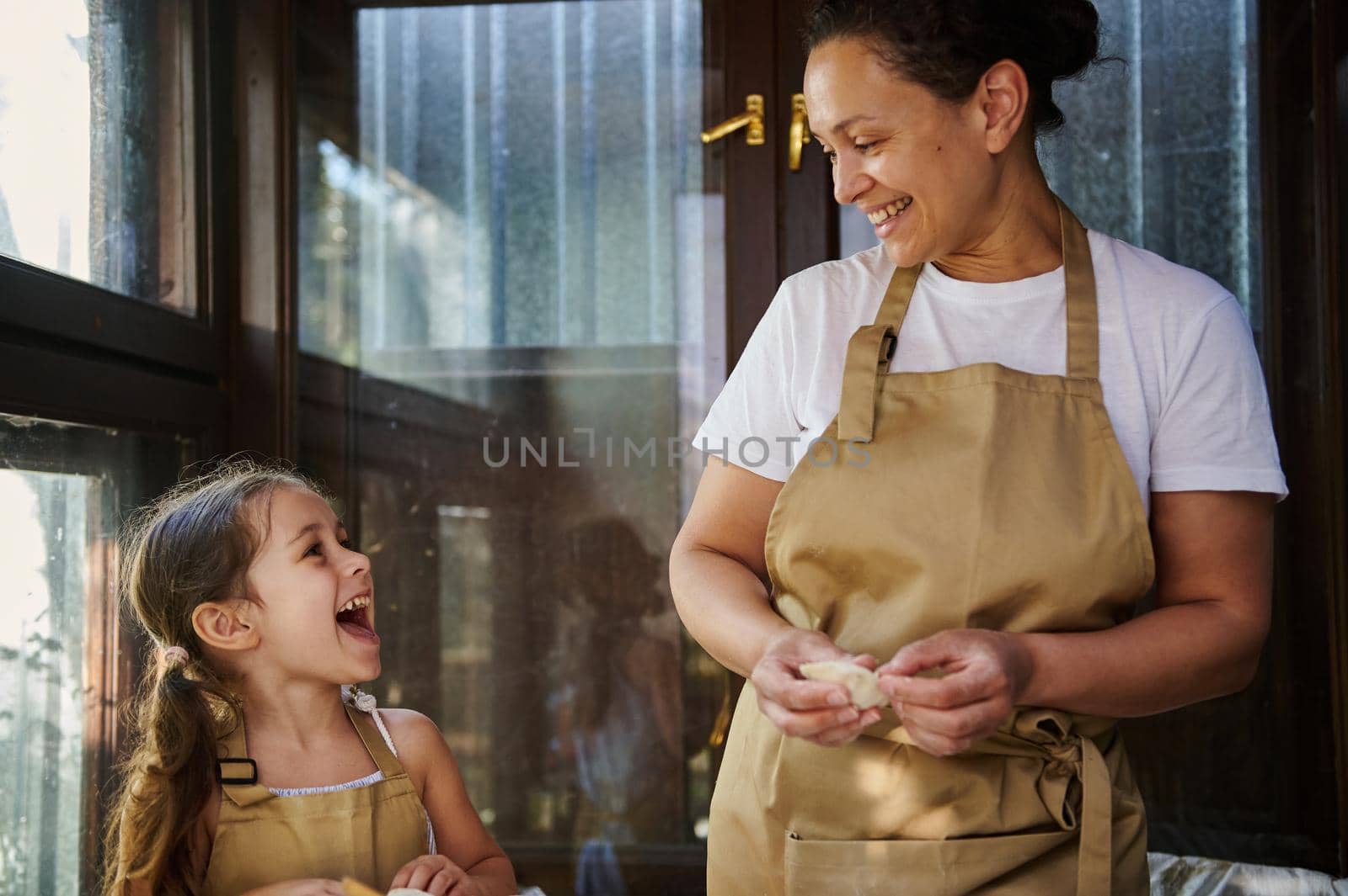 Happiness is spending time with mom. Loving mother and her cute little daughter cooking delicious homemade dumplings together in a country kitchen. Scene of artisanal food preparation. Baking concept