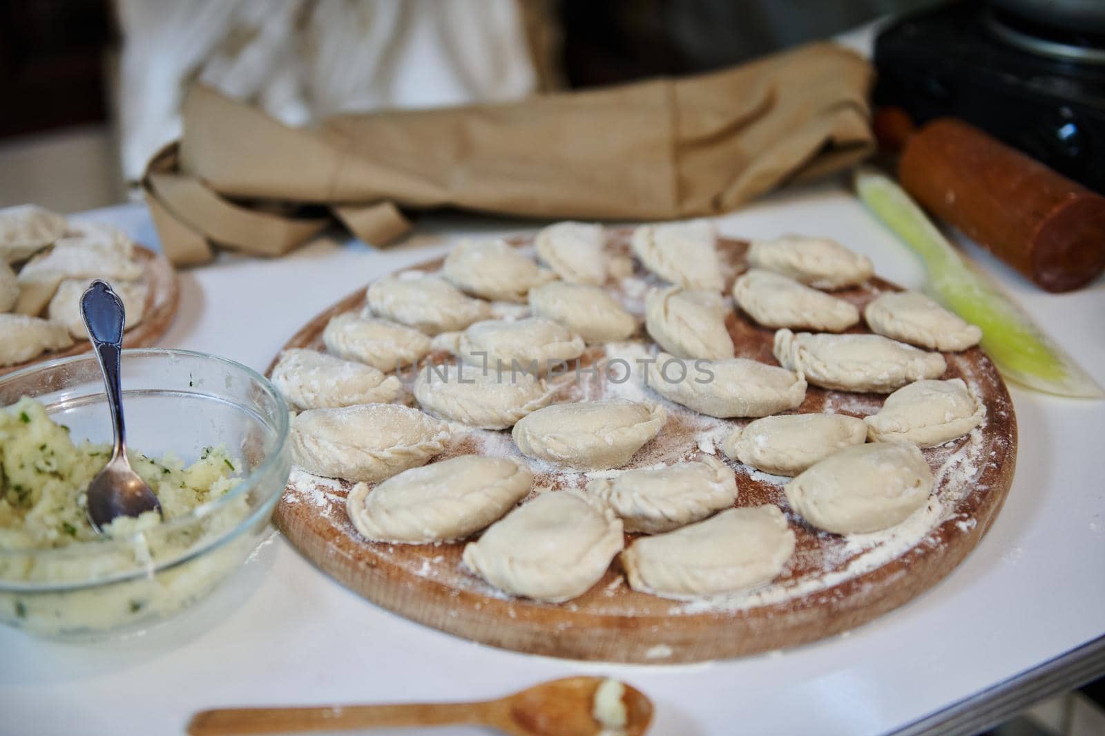 Selective focus on homemade dumplings, Ukrainian varenyky sprinkled with wholegrain flour, on a wooden board in the rustic summer country kitchen. National dish in Ukraine. Dumplings Pelmeni Ravioli