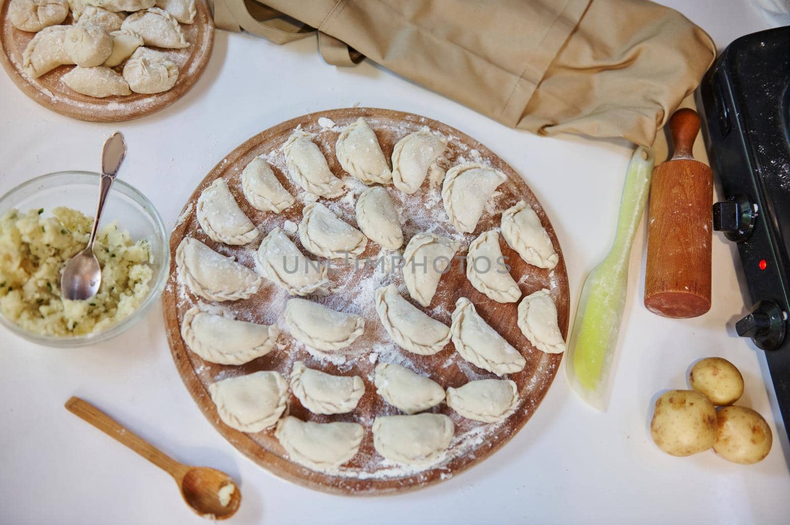 Top view. Rustic kitchen table with uncooked dumplings stuffed with mashed potatoes and sprinkled with flour on a wooden cutting board with ingredients. Traditional Ukrainian dish - Varenyky