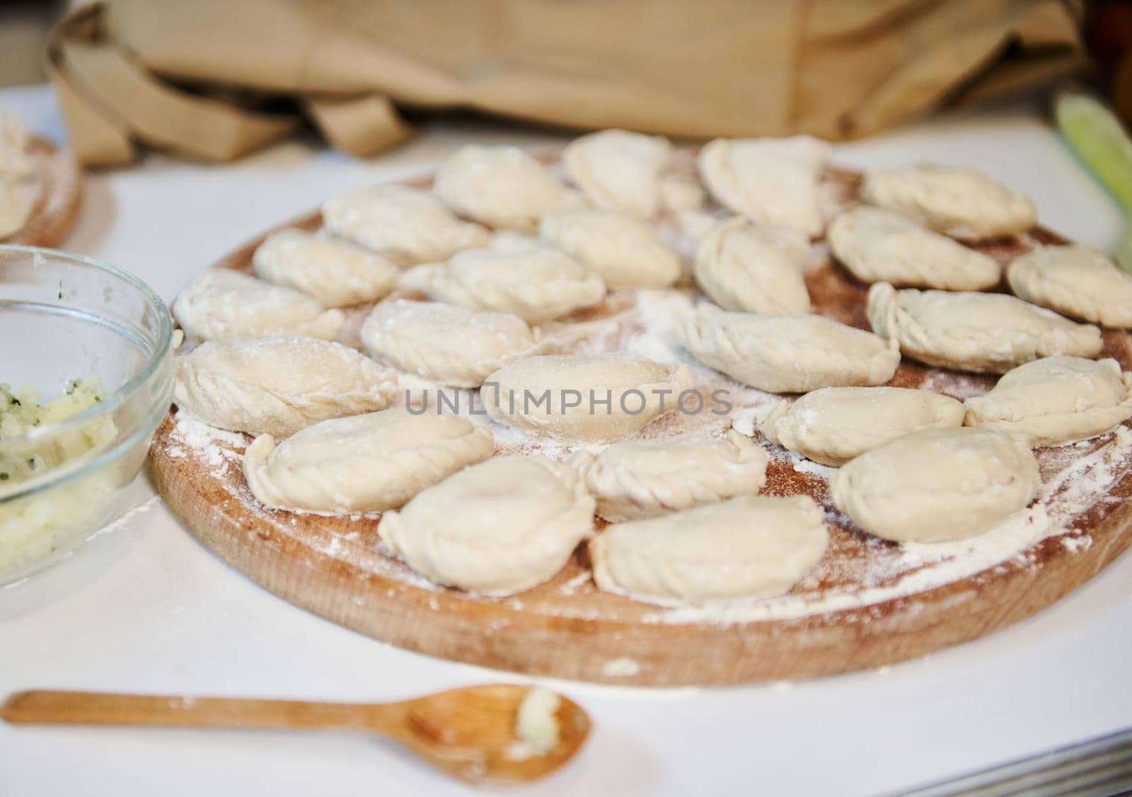 Selective focus on homemade dumplings, Ukrainian varenyky sprinkled with wholegrain flour, on wooden board, prepared according to traditional recipe. National dish in Ukraine. Russian Pelmeni. Ravioli