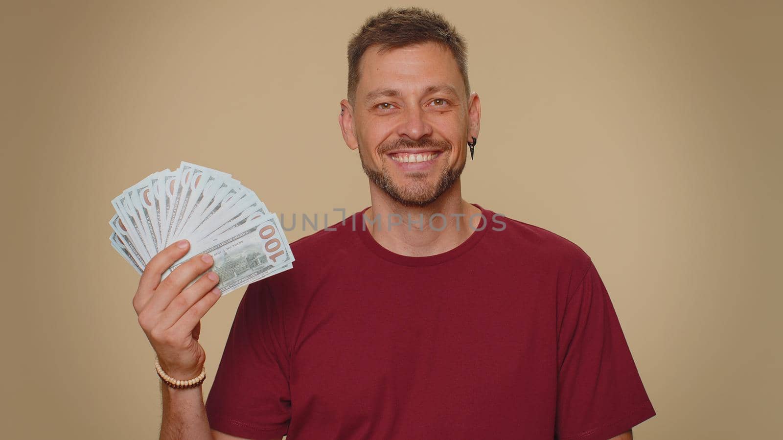 Rich pleased boss handsome young man waving money dollar cash banknotes bills like a fan, success business career, lottery winner, big income, wealth. Adult stylish guy isolated on beige background