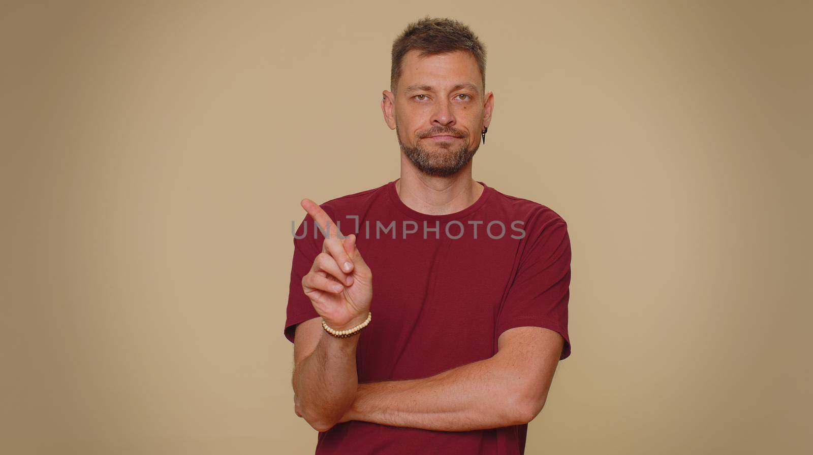 Offended handsome young man having misunderstanding, frustrated after quarrel, ignores and does not want to communicate, talk. Adult stylish male guy isolated on beige studio background indoors