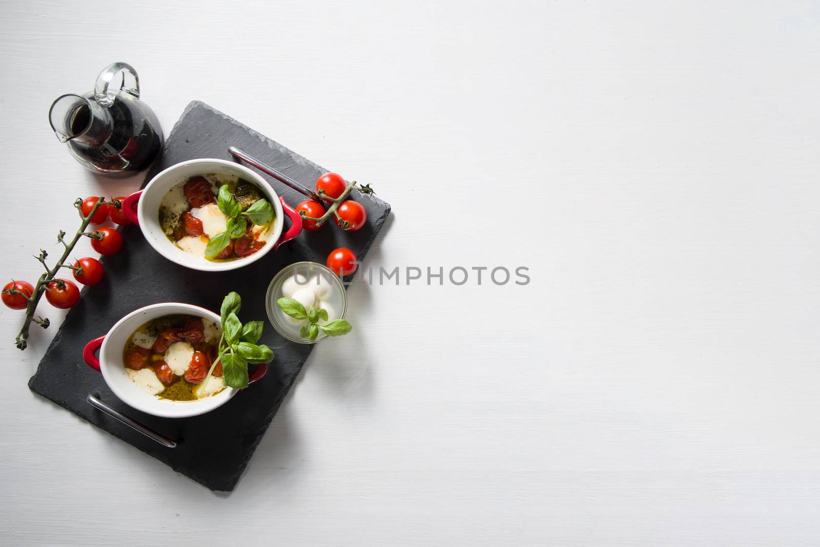 Italian caprese salad, baked cherry tomatoes, mozzarella and basil on a white table, still life, flat lay, copy space