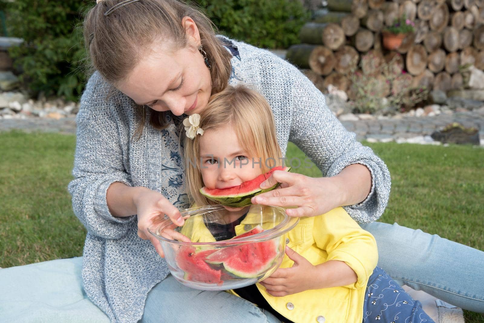 young mother feeds her daughter sweet watermelon, picnic in nature near the house.High quality photo