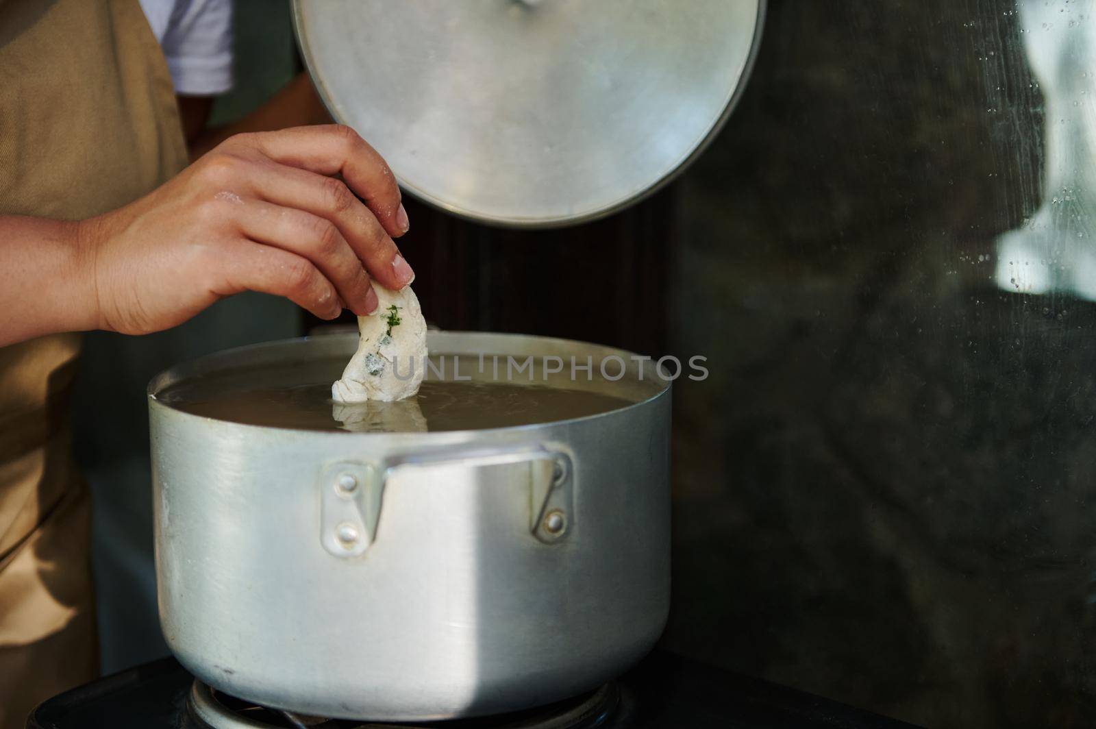 Close-up housewife dipping raw dumplings into a boiling water, brewing Ukrainian vareniki. by artgf