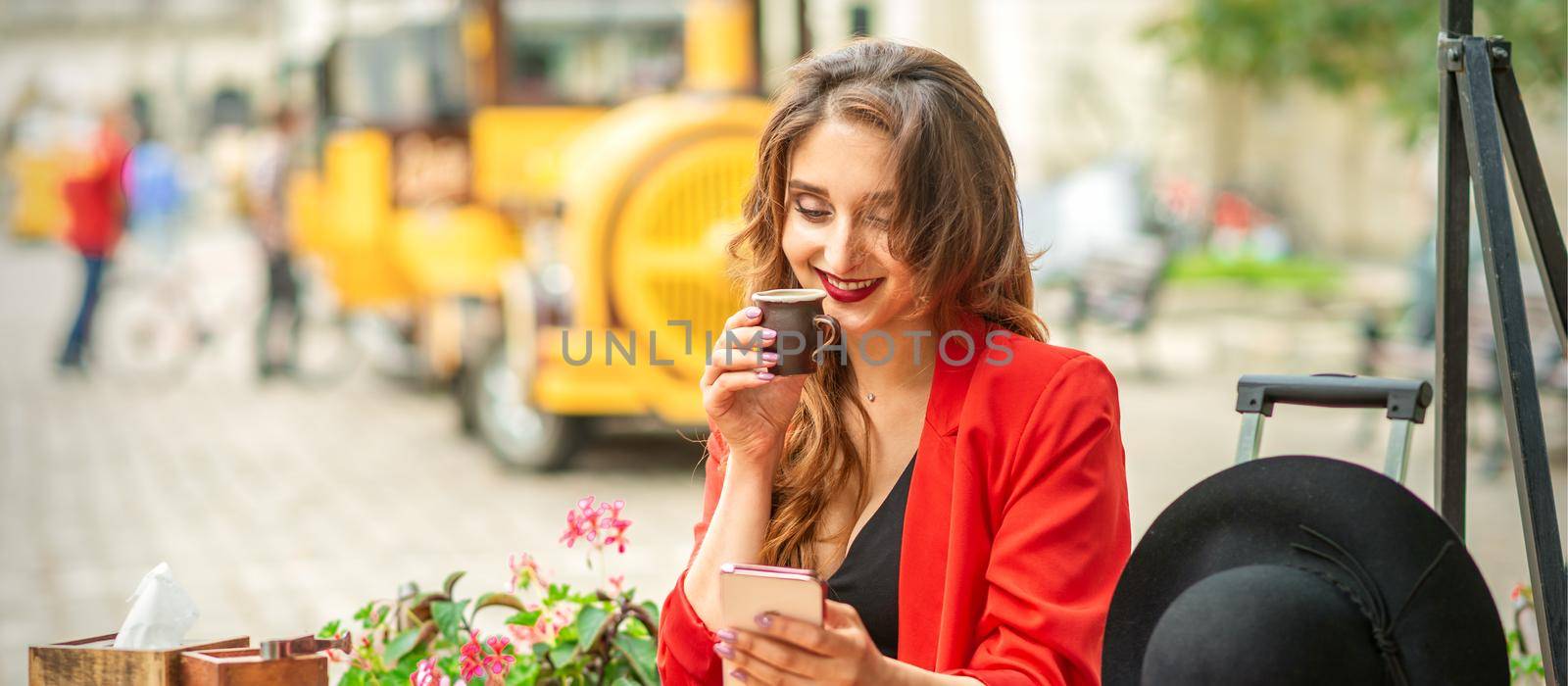 Tourist young caucasian woman in red jacket with coffee cup at the table in cafe outdoors