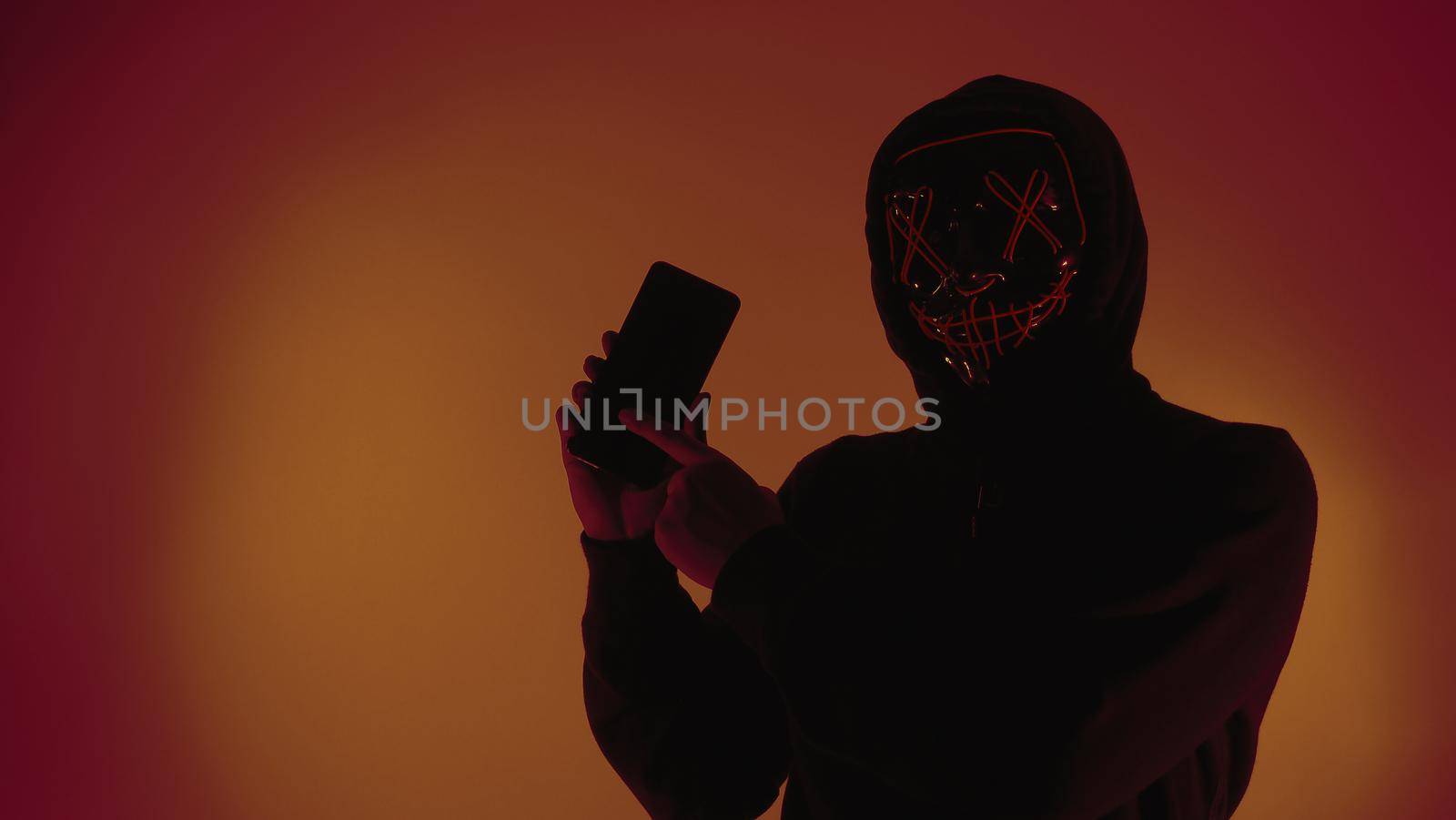 Digital security Concept. Anonymous hacker with mask holding smartphone hacked. Personal and Cyber data security in mobile phone stolen by man in mask. Represent digital privacy protection concept.