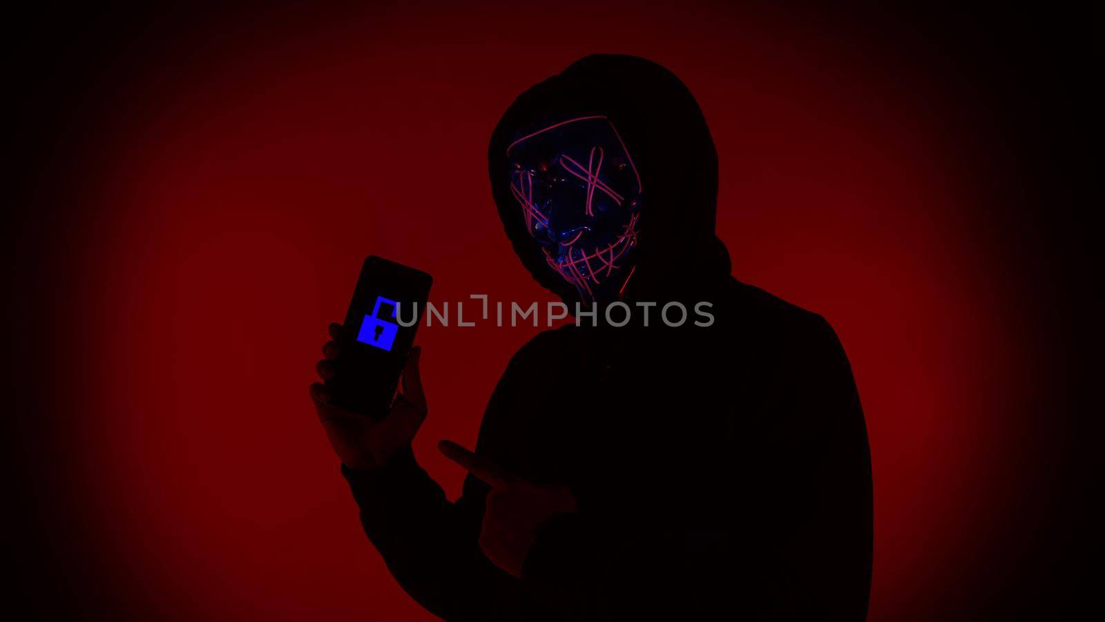 Digital security Concept. Anonymous hacker with mask holding smartphone hacked. by gnepphoto