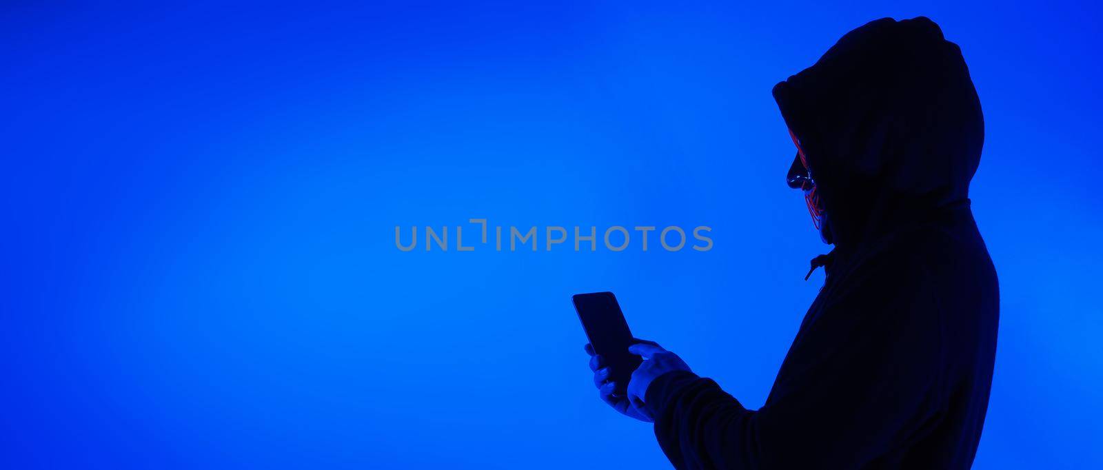 Digital security Concept. Anonymous hacker with mask holding smartphone hacked. by gnepphoto