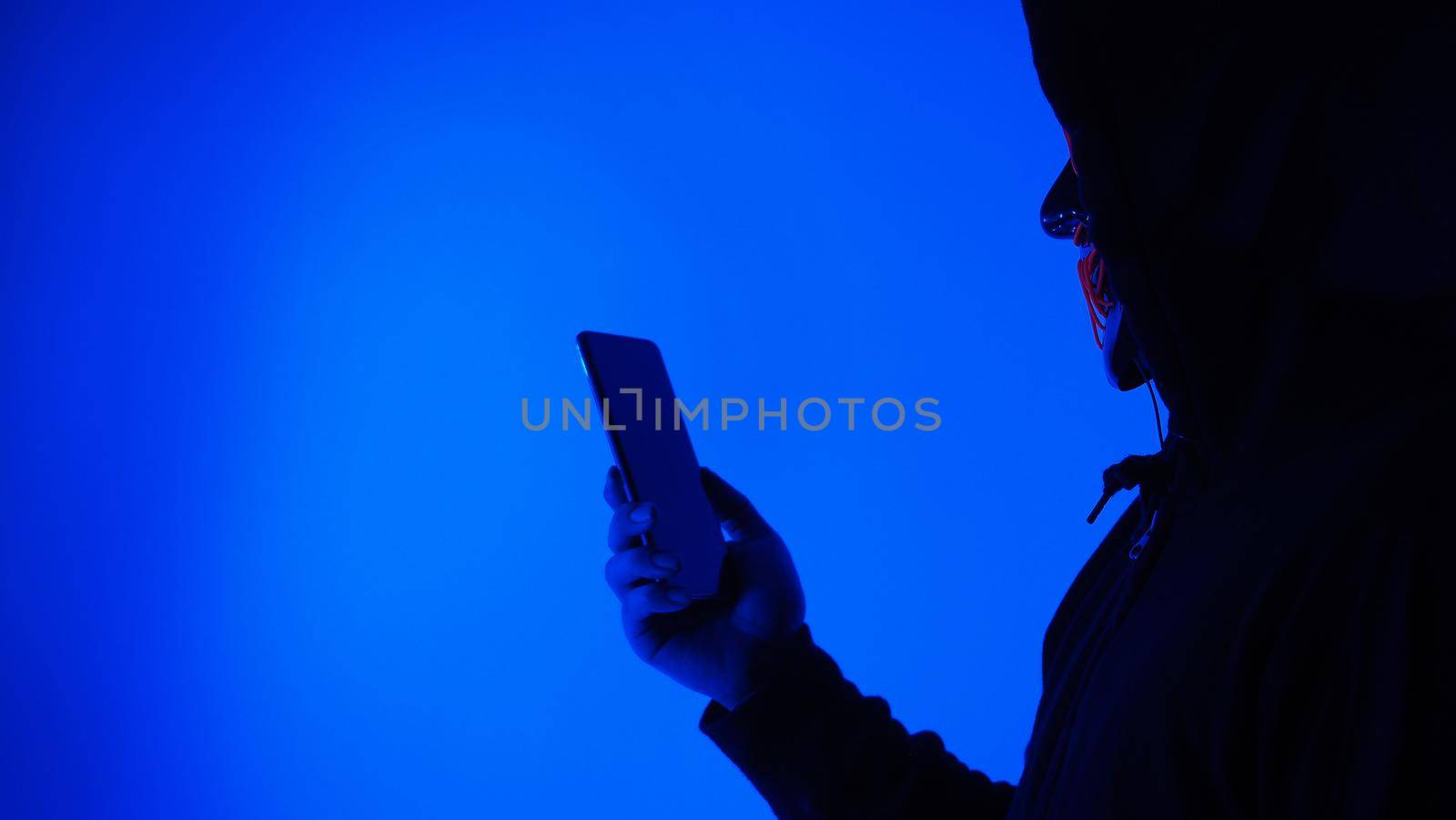 Digital security Concept. Anonymous hacker with mask holding smartphone hacked. by gnepphoto