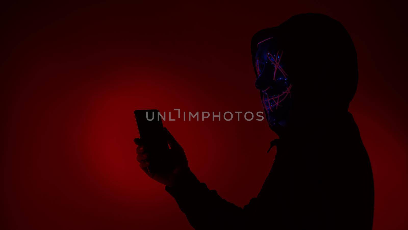 Digital security Concept. Anonymous hacker with mask holding smartphone hacked. Personal and Cyber data security in mobile phone stolen by man in mask. Represent digital privacy protection concept.