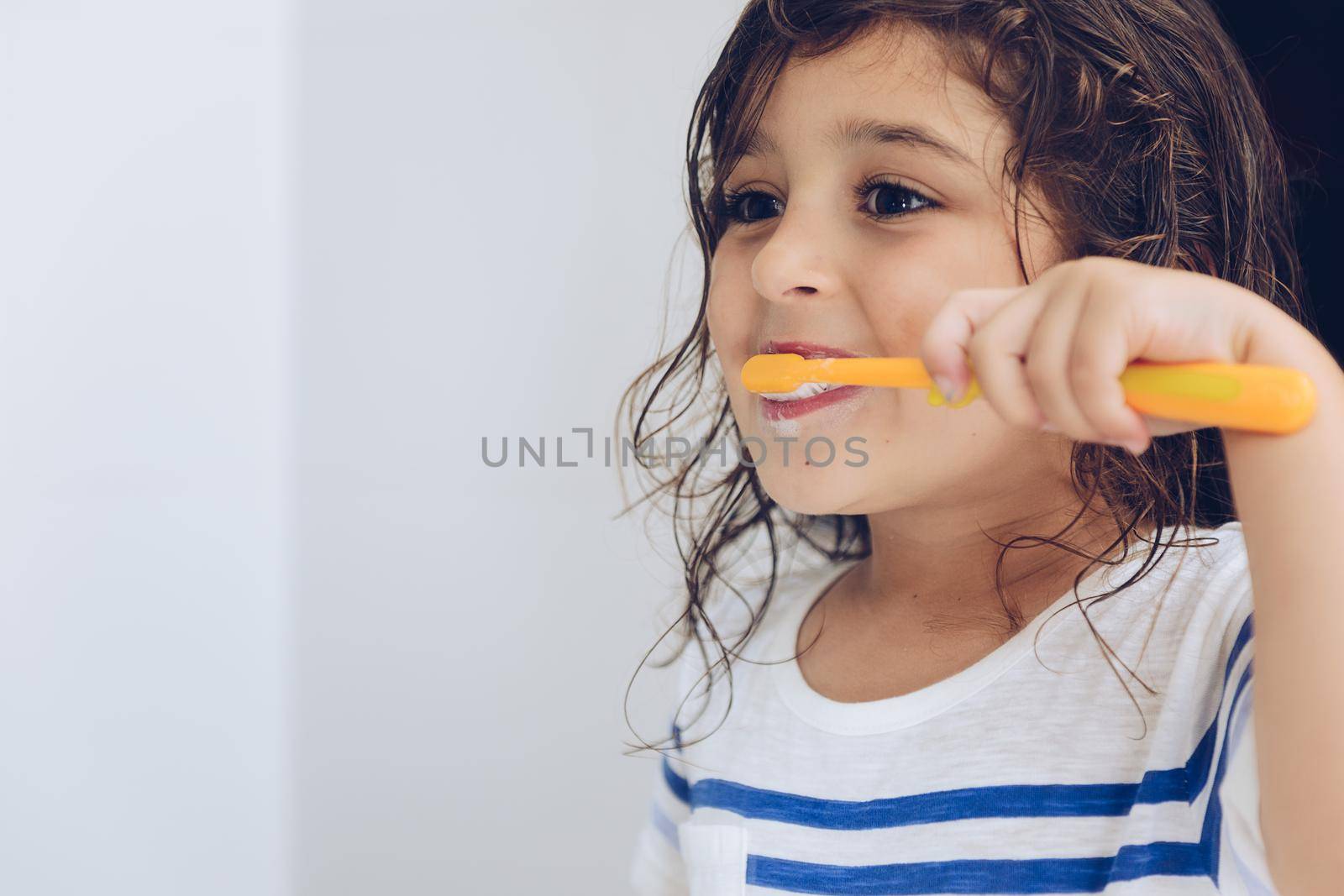 portrait of a little girl brushing her teeth in the bathroom before going to bed after shower, kids hygiene concept, copy space for text
