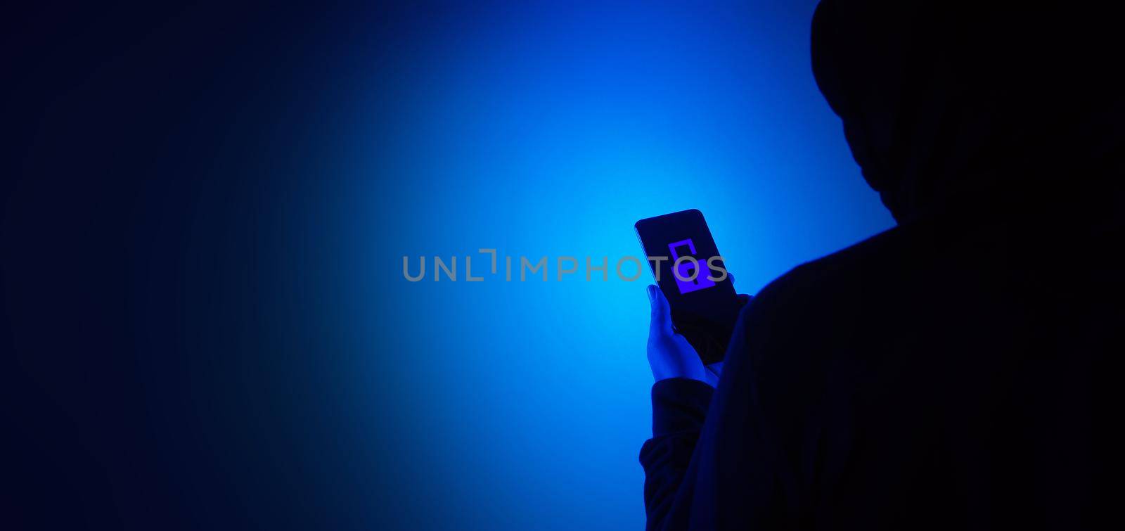 Digital security Concept. Anonymous hacker with mask holding smartphone hacked. by gnepphoto