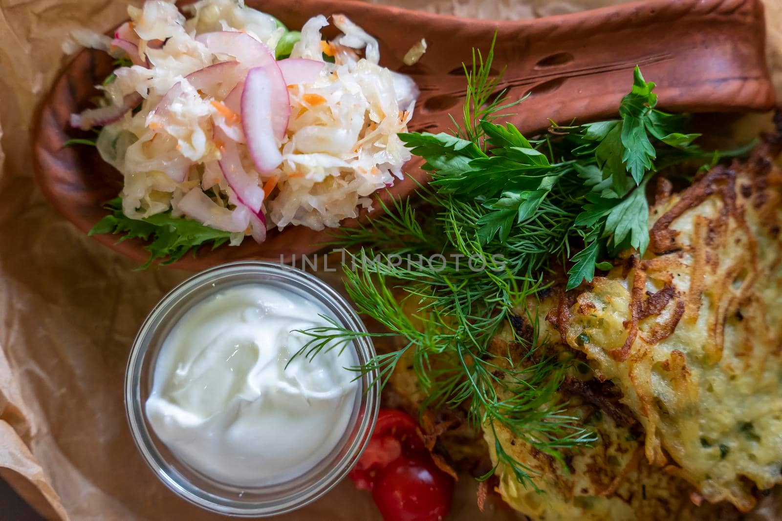 Draniki served with sour cream, herbs and sauerkraut in the restaurant. Potato pancakes (draniki) in a plate on a wooden table.Close-up, selective focusing