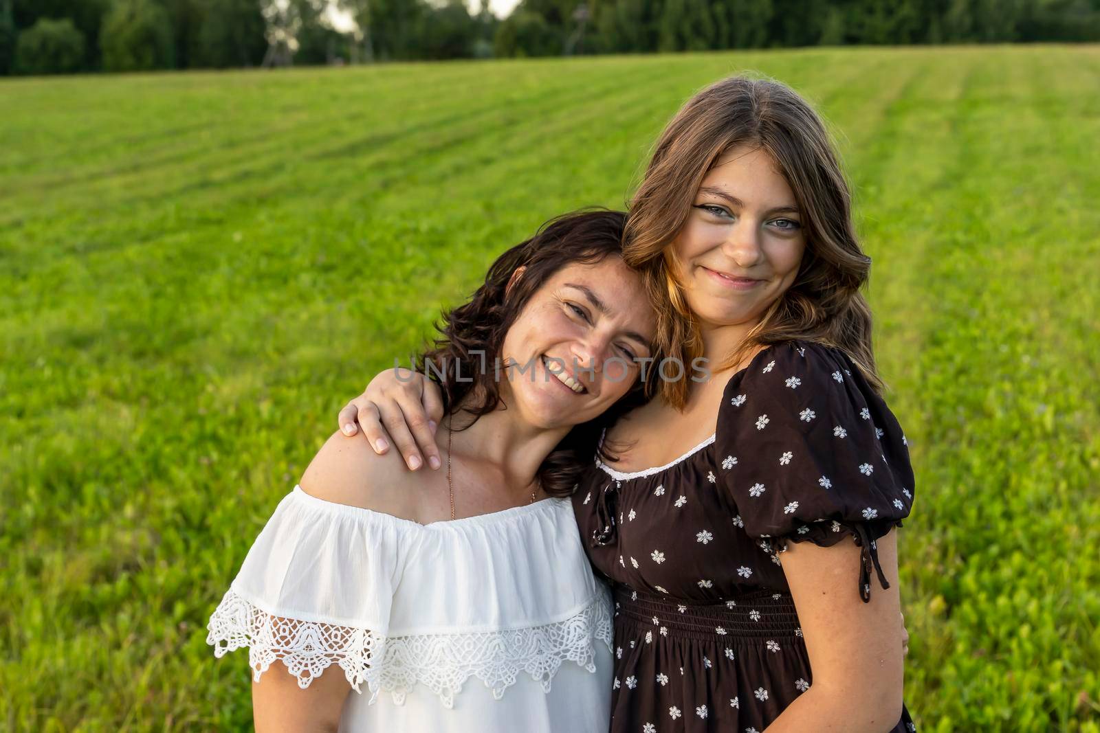 happy mom hugs her teenage daughter against a green field by audiznam2609