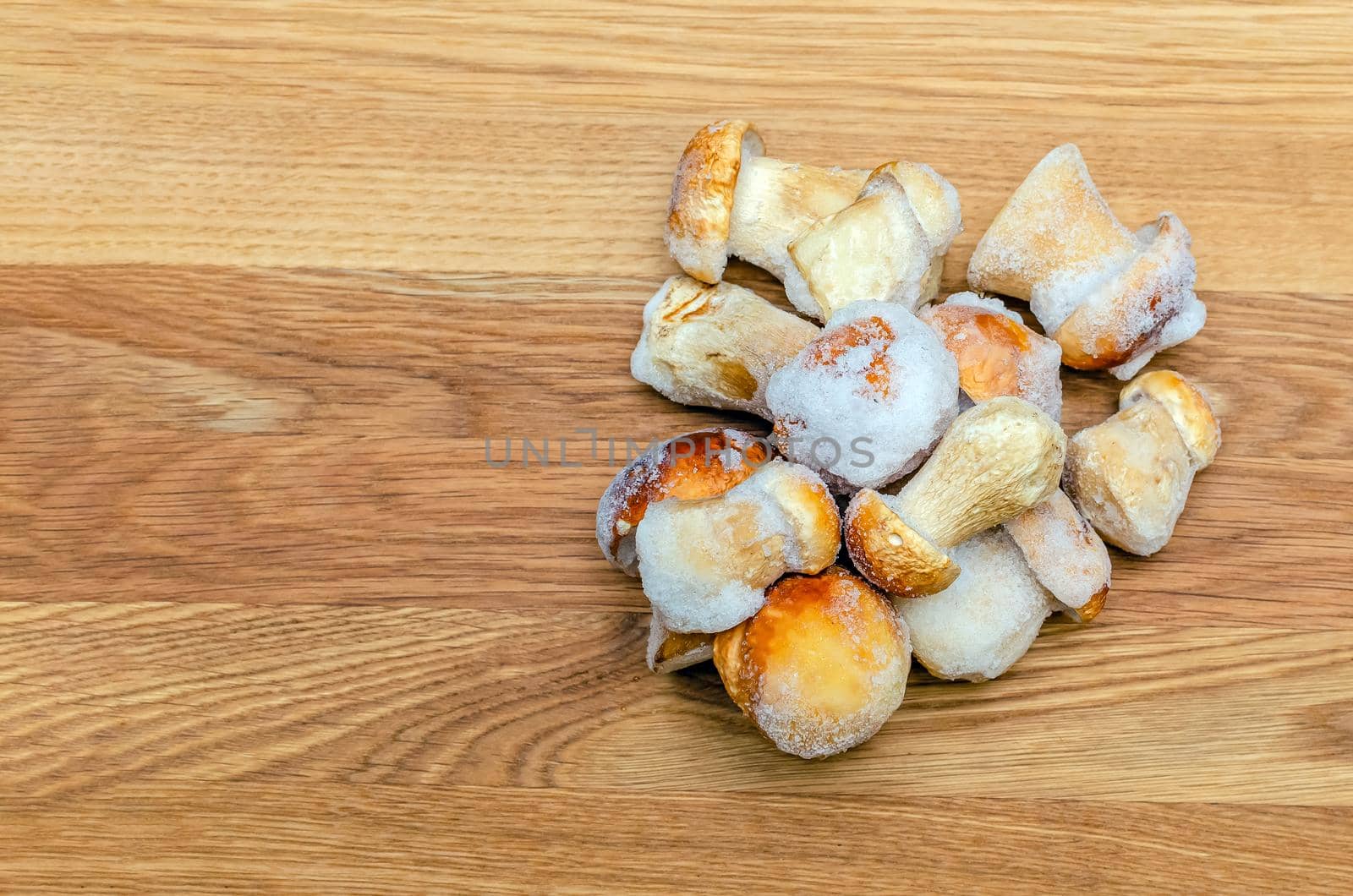 Frozen mushrooms on a wooden background. The whole boletus is frozen in the freezer