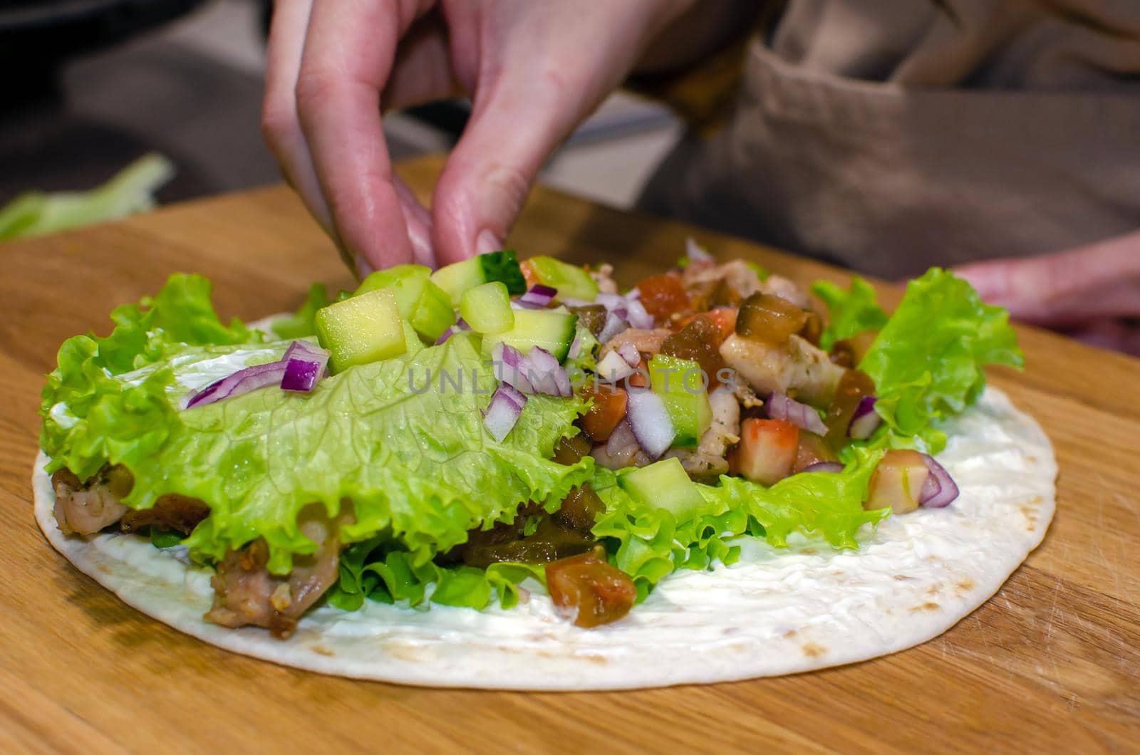 Delicious lavash rolls with fried chicken and vegetables on a wooden cutting board. Cooking process, close-up