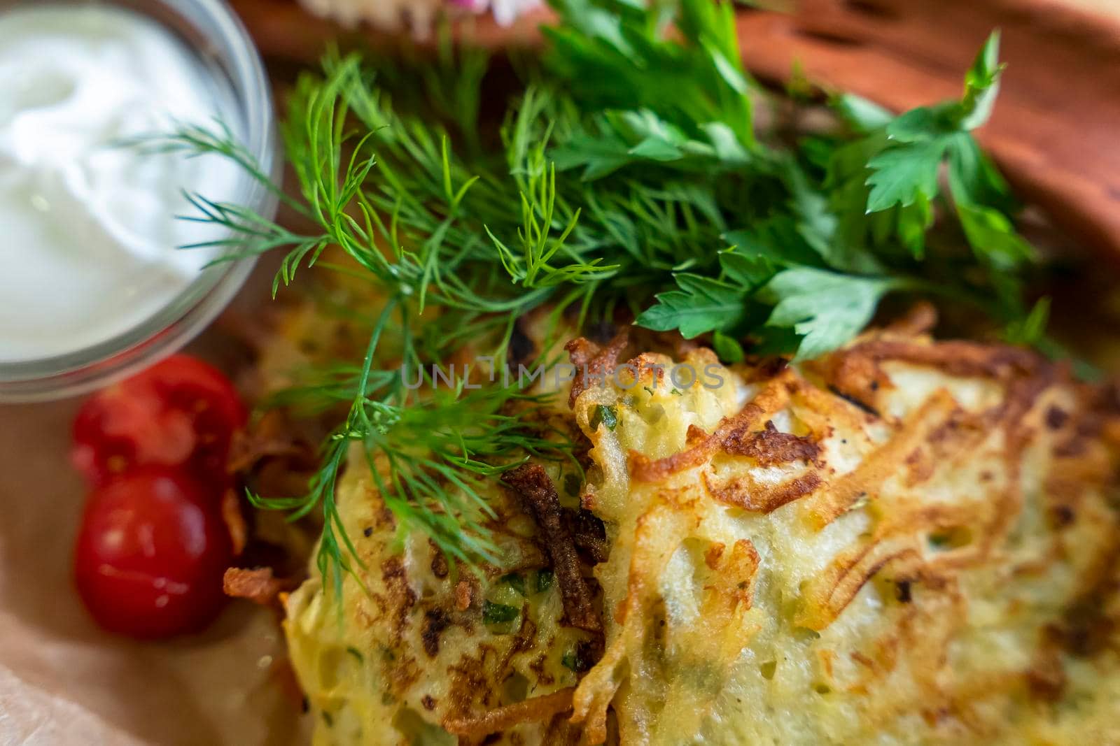 Draniki served with sour cream and herbs in the restaurant. Potato pancakes (draniki) in a plate on a wooden table.Close-up, selective focusing