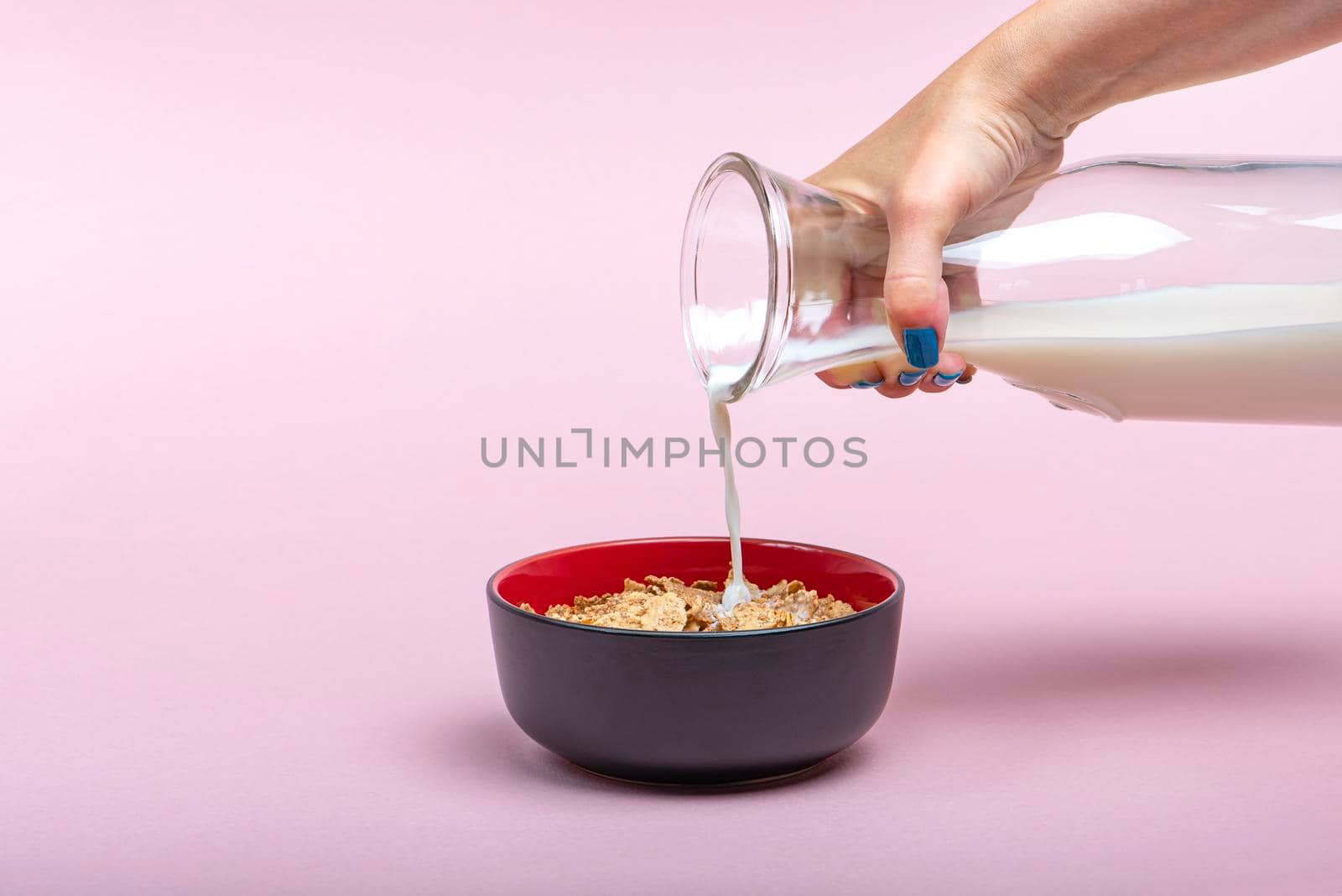 Cooking muesli. A woman pours milk from a jug into a saucer with muesli flakes. Pink background with place to insert text. Large banner for print or advertising.